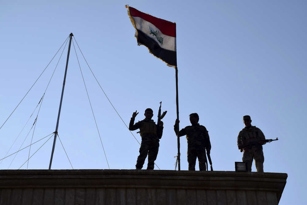 In this Monday, Dec. 21, 2015 photo, Iraqi soldiers plant the national flag over a government building in Ramadi as security forces advance their position in northern Ramadi, 70 miles (115 kilometers) west of Baghdad, Iraq. Iraqi forces on Tuesday reported progress in the military operation to retake the city of Ramadi from the Islamic State group, saying they made the most significant incursion into the city since it fell to the militants in May. (AP Photo)