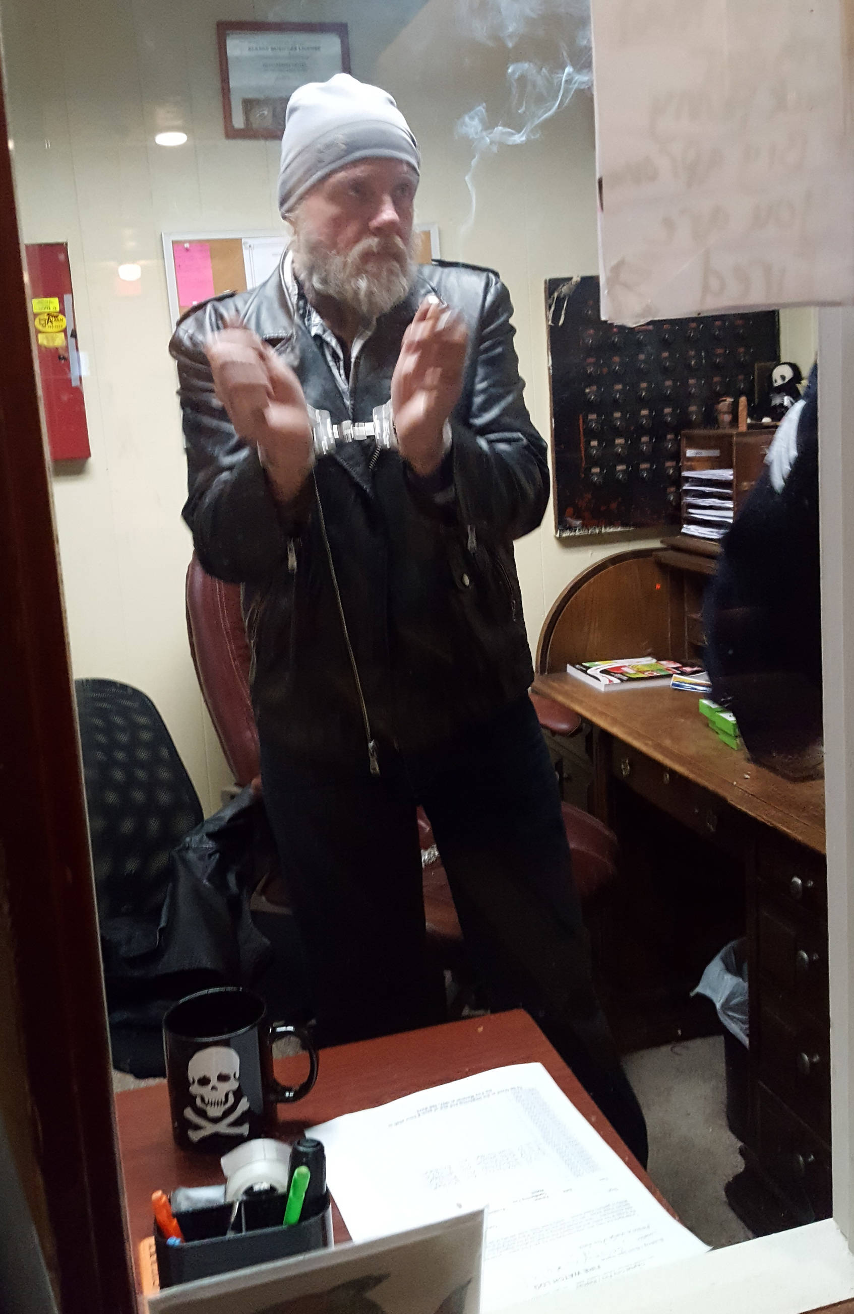 Bergmann Hotel manager Charles Cotten displays his handcuffs as he waits to be taken to jail Friday afternoon. (Liz Kellar | Juneau Empire)