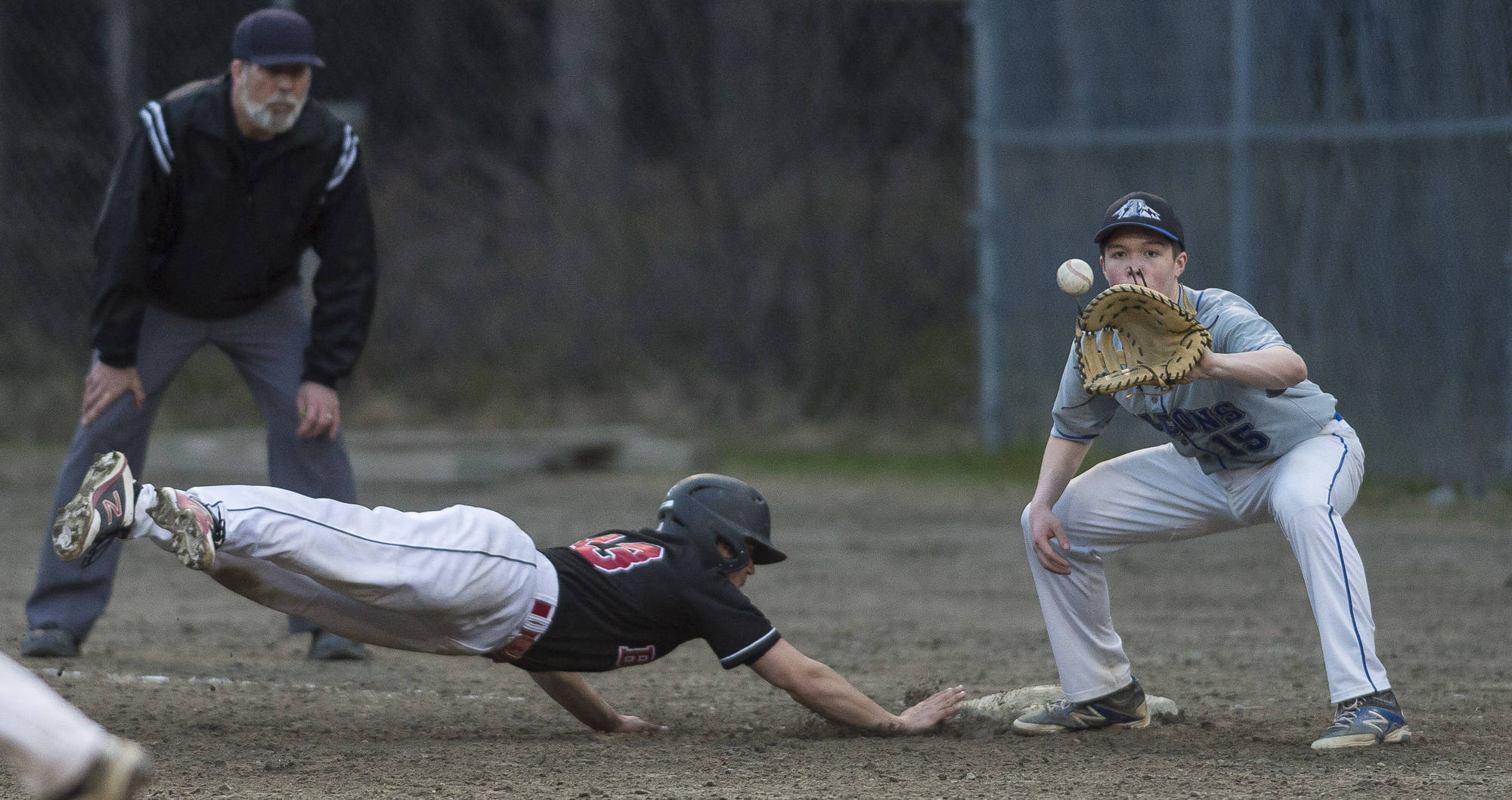 Juneau-Douglas’ Mike Cesar dives back to first base as Thunder Mountain’s Sammy McKnight takes a pickoff throw from Gabe Storie at Adair-Kennedy Memorial Park on Tuesday. JDHS won 13-12. (Michael Penn | Juneau Empire)