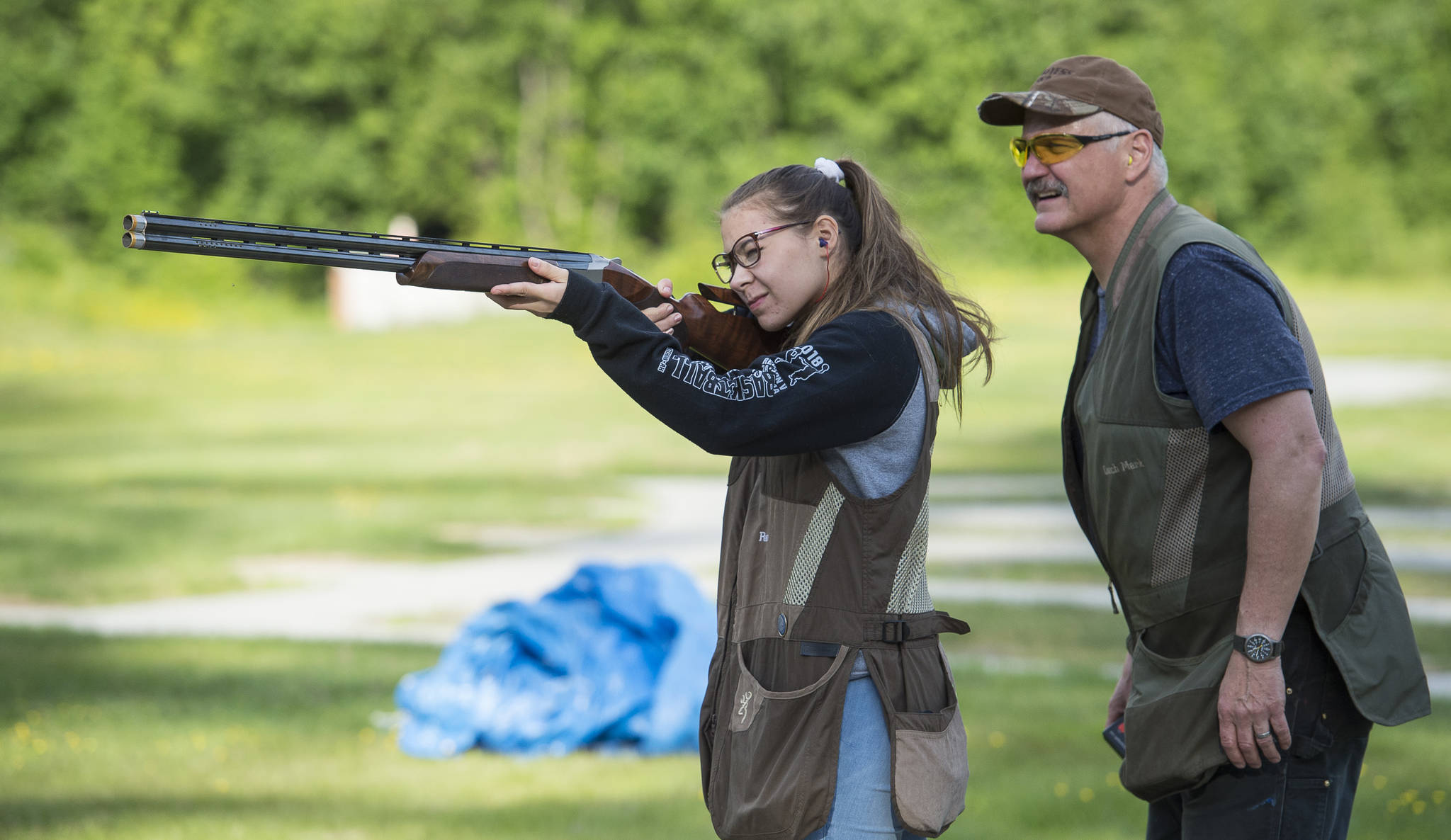 Coach Mark Kappler watches as Renee Win practices her trap shooting at the Juneau Gun Club on Thursday. (Michael Penn | Juneau Empire)