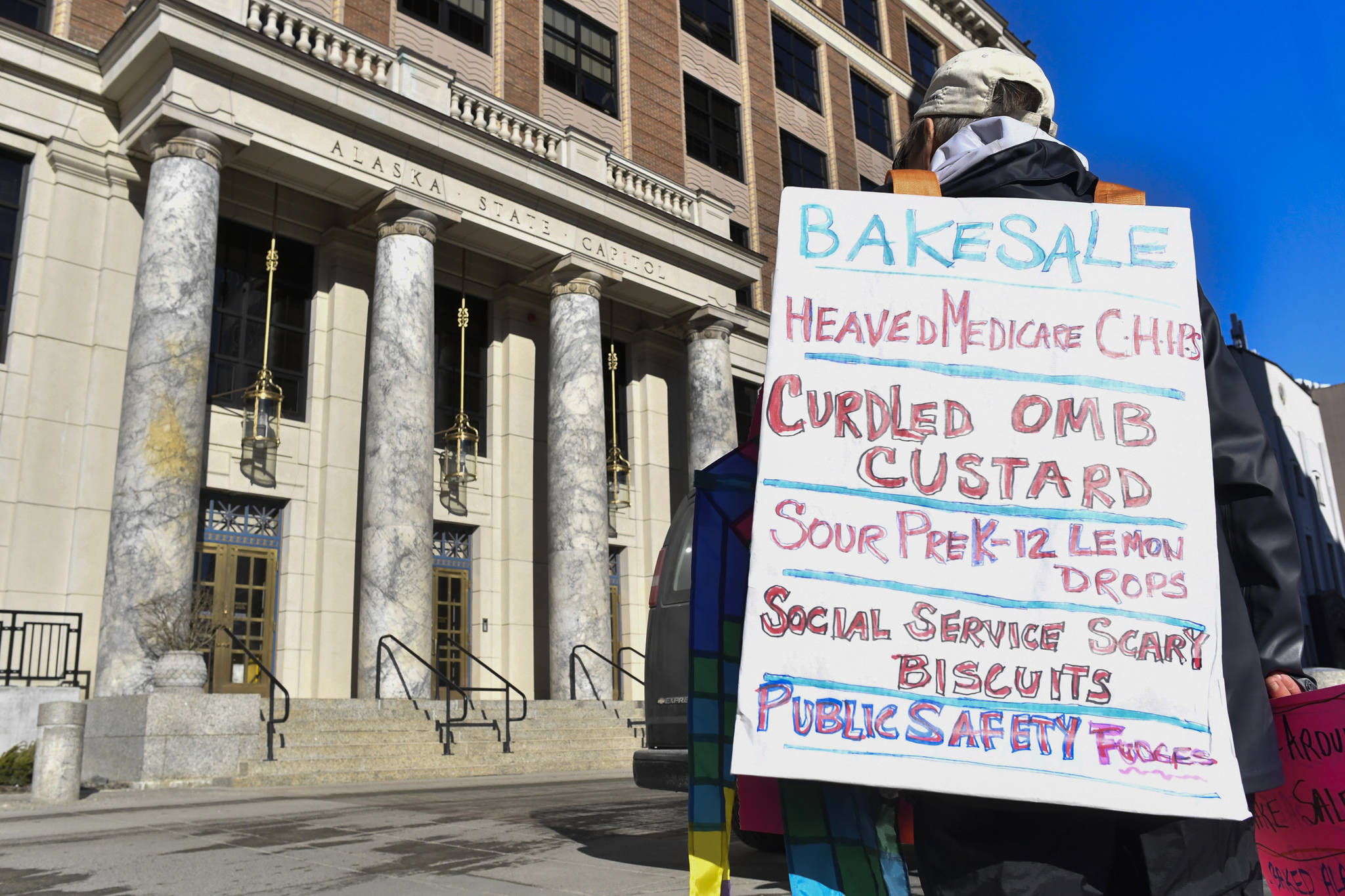 Lin Davis holds a protest against Gov. Mike Dunleavy’s state budget proposals with a sandwich board of potenial menu items in front of the Capitol on March 7, 2019. (Michael Penn | Juneau Empire File)