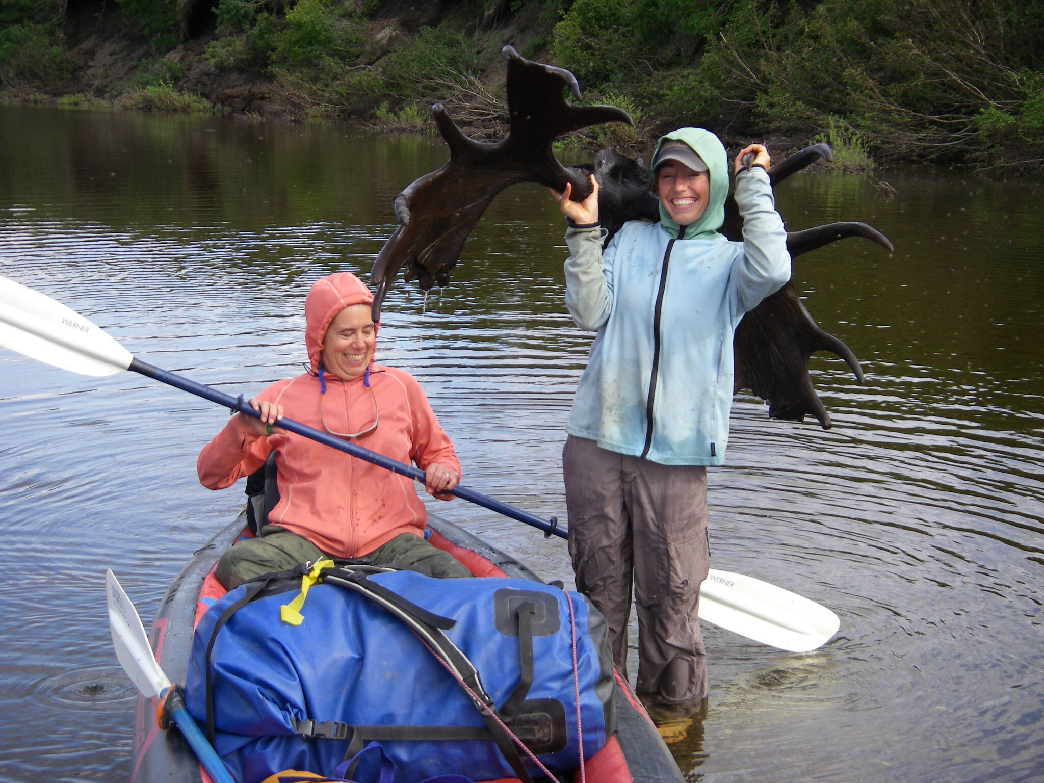 Molly Yazwinski holds a 3,000-year-old moose skull with antlers still attached, found in a river on Alaska’s North Slope. Her aunt, Pam Groves, steadies an inflatable canoe. (Courtesy Photo /Dan Mann)