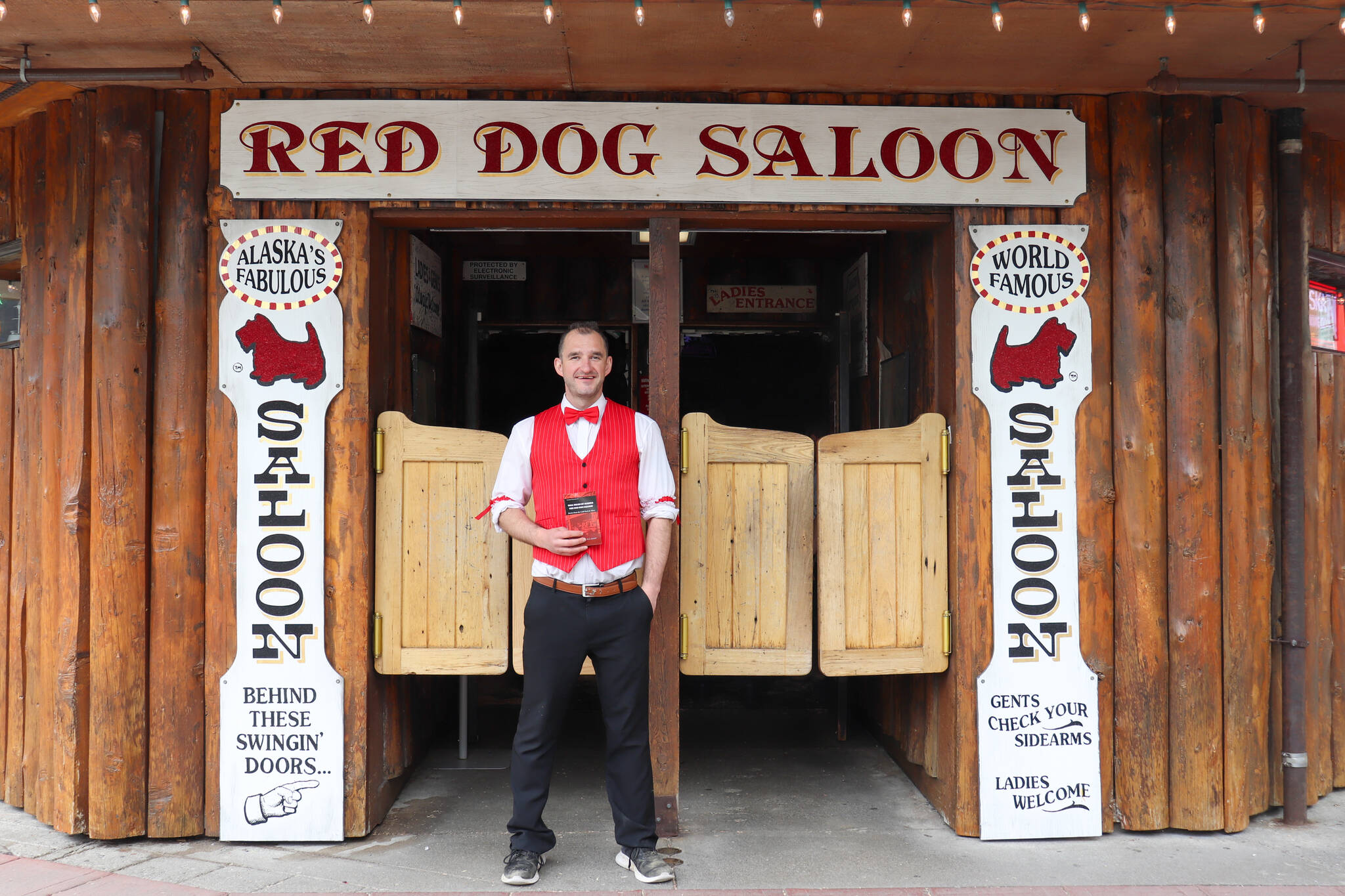 Juneau author W.R. Kozey holds his book “Tall Tales of Alaska, The Red Dog Saloon: Stories from the Gold Rush & More” in front of the Red Dog Saloon on Sunday. (Jasz Garrett / Juneau Empire)
