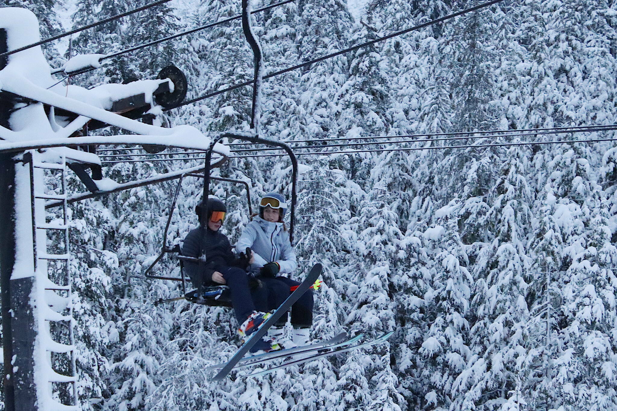 Two skiers settle into a lift chair as they pass trees with fresh snow at Eaglecrest Ski Area on Dec. 20, 2023. (Mark Sabbatini / Juneau Empire file photo)