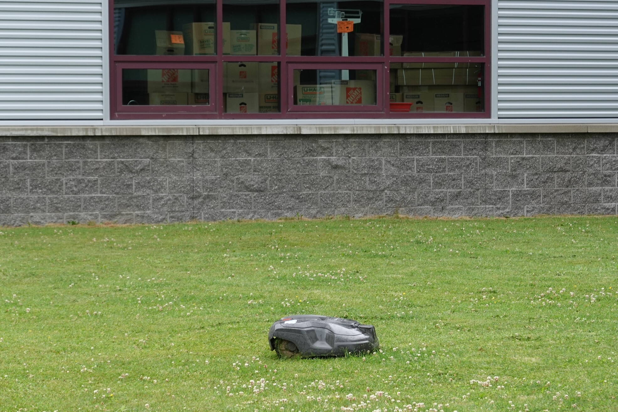 Looking like a gray turtle, an automated mower cuts grass in front of Thunder Mountain Middle School with boxes stacked in a classroom window beyond. (Laurie Craig / Juneau Empire)