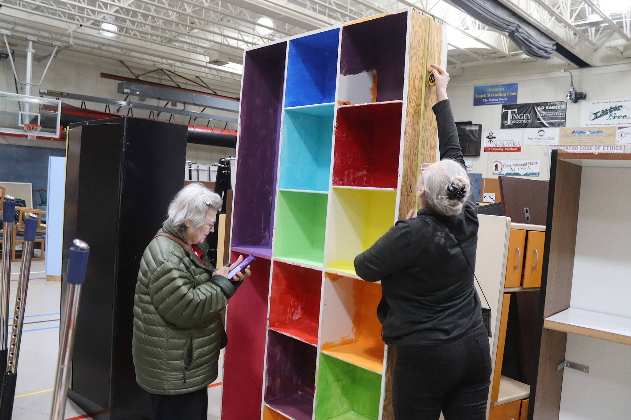 Shelley McNurney (right) and Tami Hesseltine examine a muticolor storage shelf in the gym of the former Floyd Dryden Middle School on Saturday, where surplus items from the school were being sold to residents and given away to nonprofit entities. (Mark Sabbatini / Juneau Empire)