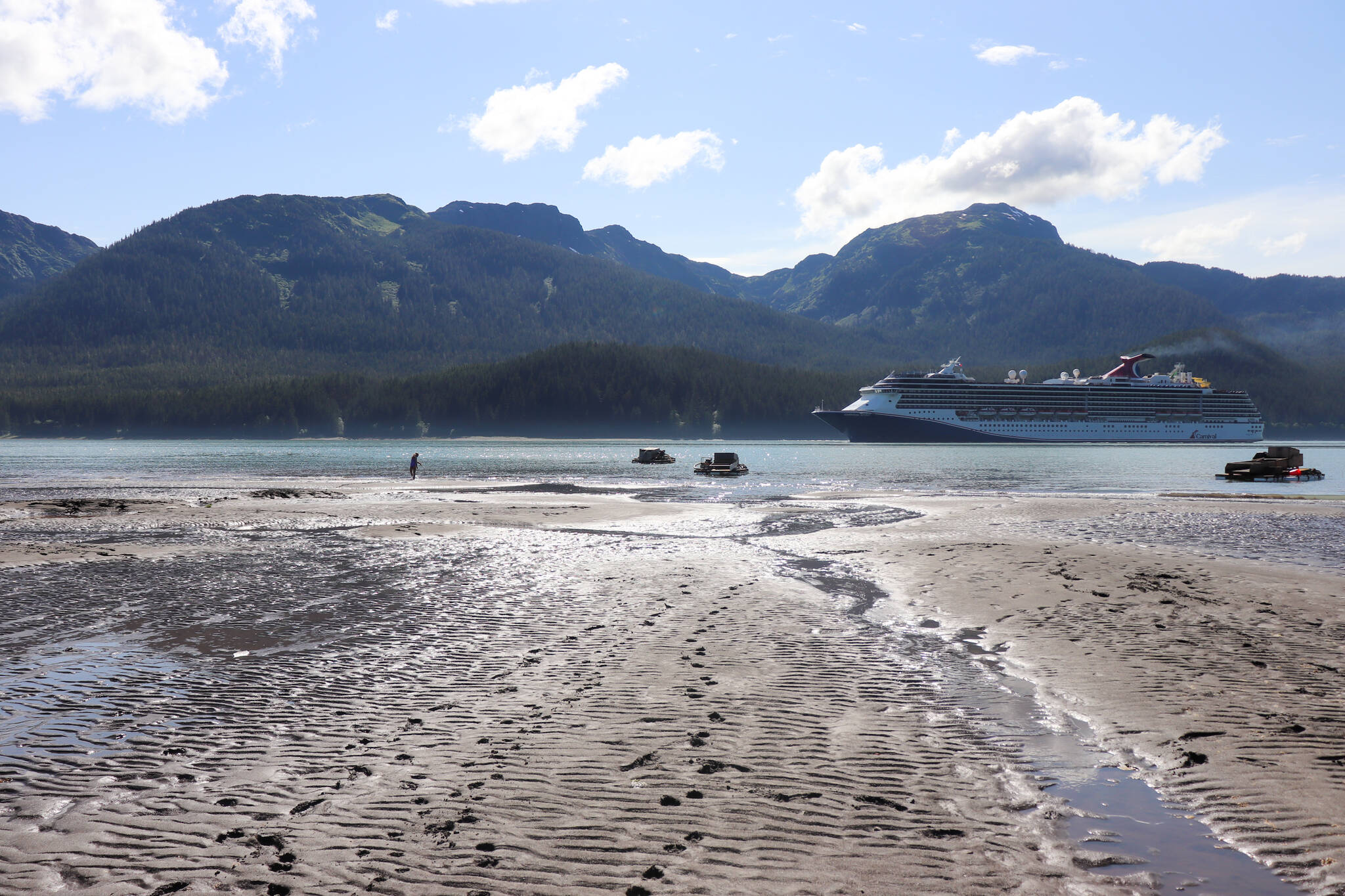 A young girl plays on the Sheep Creek delta near suction dredges while a cruise ship passes the Gastineau Channel on July 20. (Jasz Garrett / Juneau Empire)