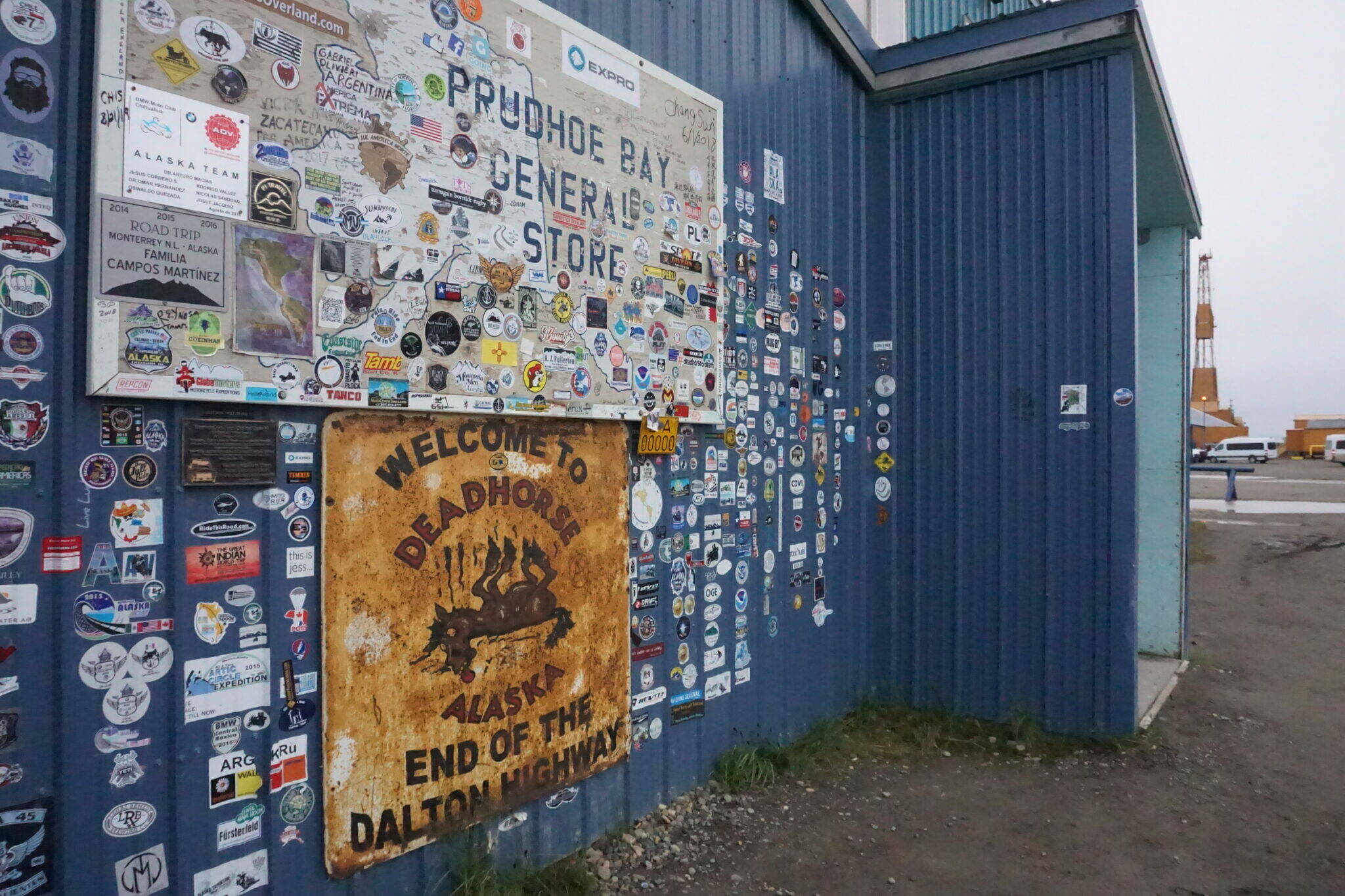 The sticker-covered wall outside the Prudhoe Bay General Store, a landmark in the community of Deadhorse, is seen on Aug. 22, 2018. Behind it is an oil equipment and oil-related facilities sited at Deadhorse, just outside of the Prudhoe Bay field. On Tuesday, temperatures reached 89 degrees at the industrial camp community, the highest ever recorded there and likely the highest ever recorded at this latitude anywhere in North America. (Yereth Rosen/Alaska Beacon)