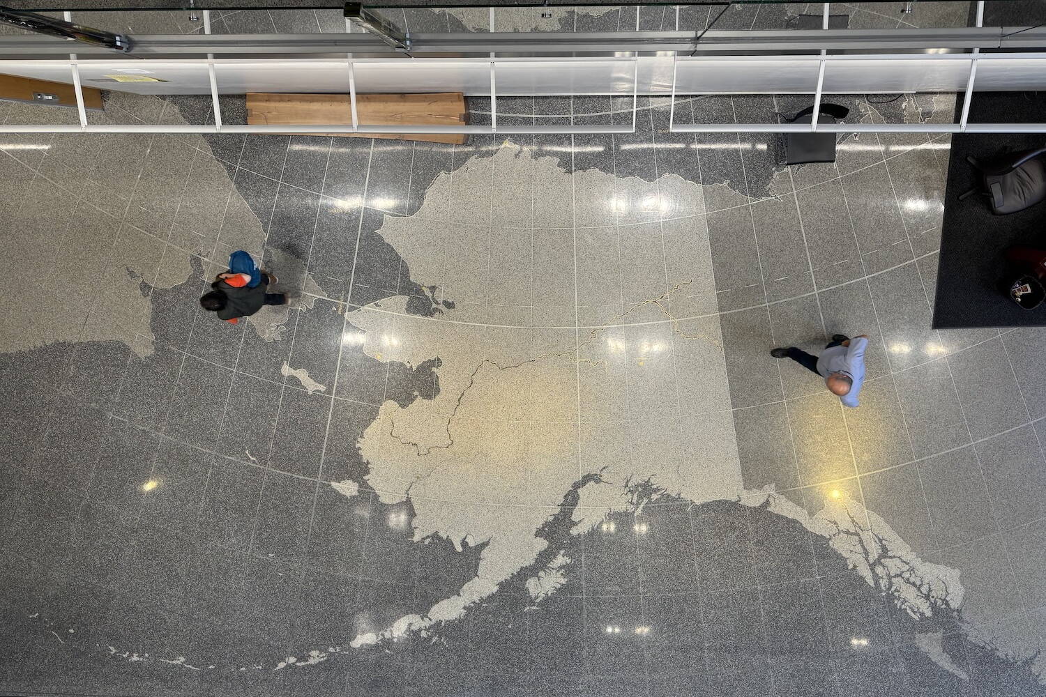 Voters walk across the map of Alaska on the floor of the Alaska State Library, Archives and Museum on Tuesday, Aug. 20, 2024. (James Brooks/Alaska Beacon)