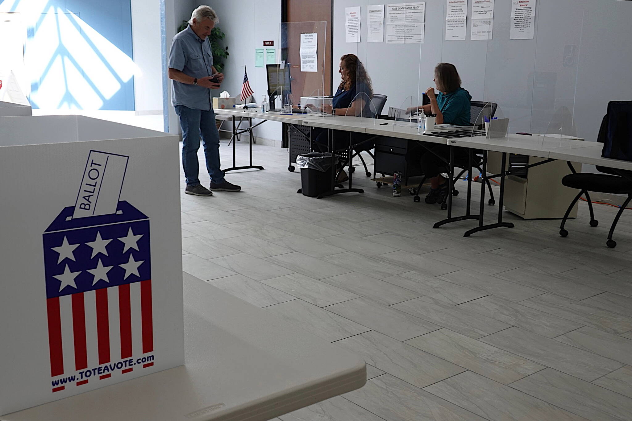 Bruce Scandling receives his ballot for Alaska’s primary election at the Mendenhall Mall Annex on Saturday morning from election officials Jackie Rosenbruch and Barb Murray. (Laurie Craig / Juneau Empire)