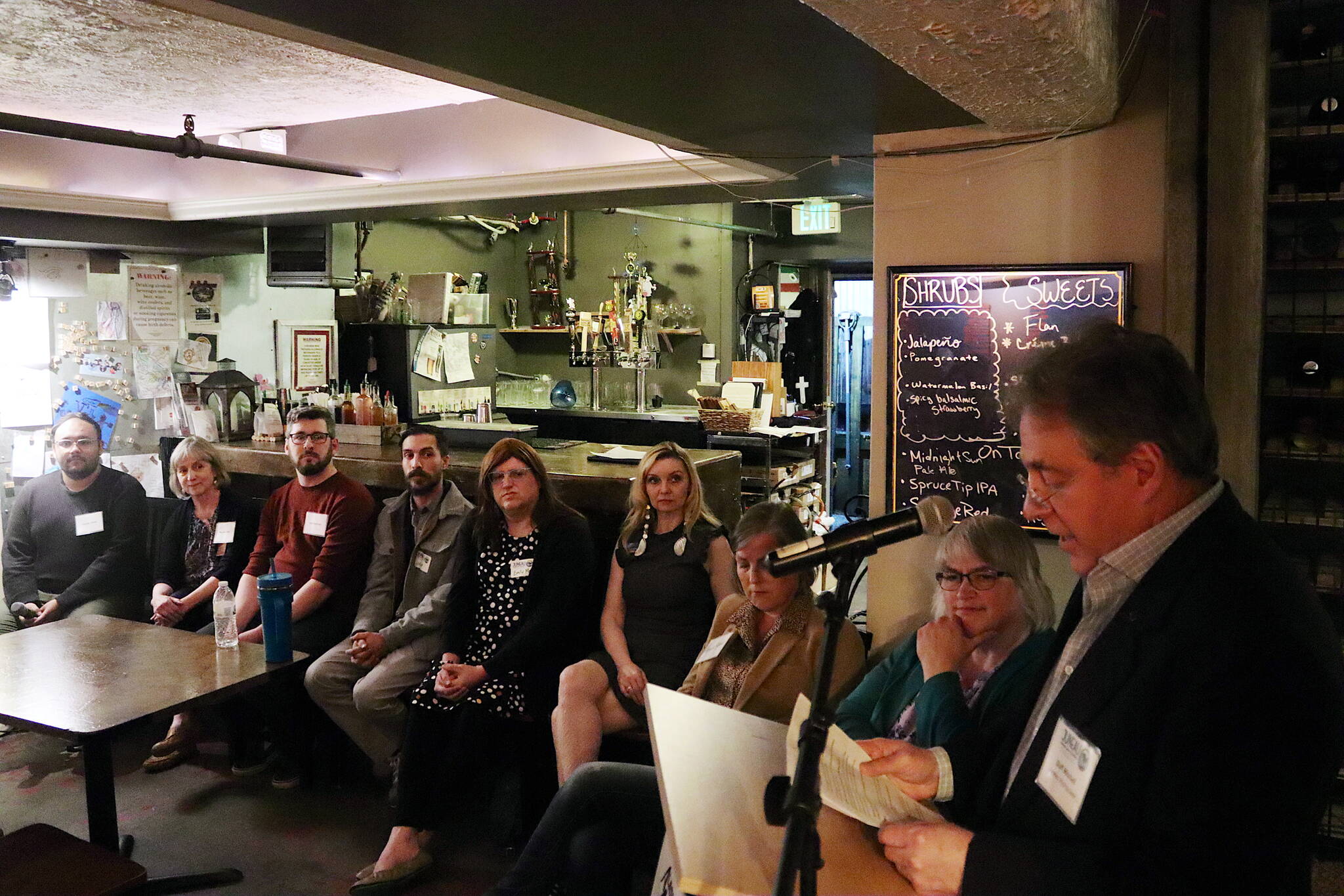 Duff Mitchell (right), a board member of the Downtown Business Association, reads a question to Juneau Assembly and mayoral candidates during a forum Tuesday night at V’s Cellar Door restaurant. (Mark Sabbatini / Juneau Empire)