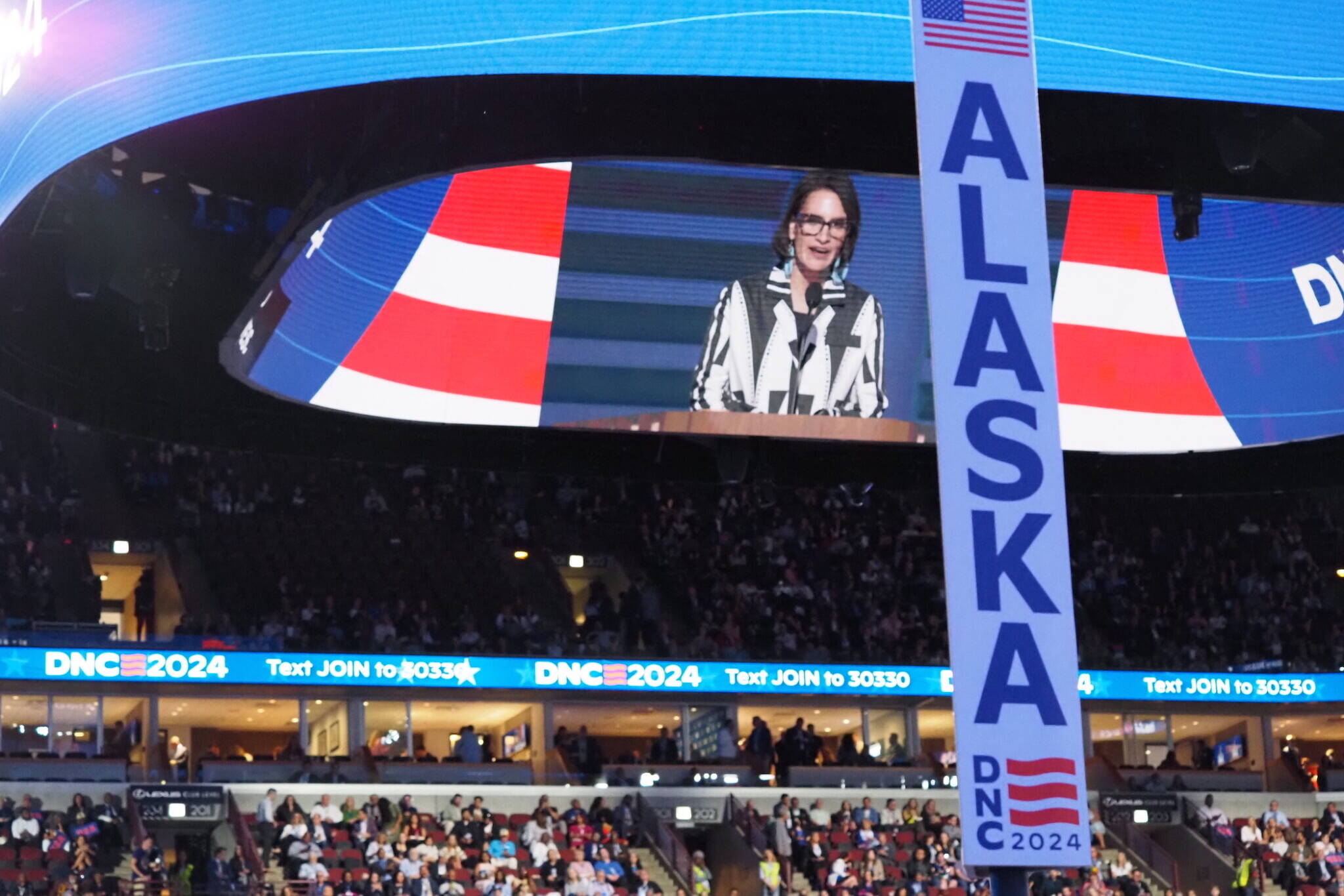 The Alaska delegation sign is seen at the Democratic National Convention on Aug. 19, 2024, in Chicago. The speaker on the screen is Minnesota Lt. Gov. Peggy Flanagan. (Ariana Figueroa/States Newsroom)