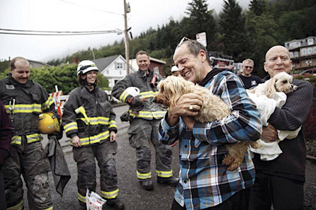 James Montiver holds Cassie, and William Montiver holds Alani behind them, members of the Ketchikan Fire Department that helped rescue the dogs on Sunday, Sept. 1, 2024. (Christopher Mullen / Ketchikan Daily News)