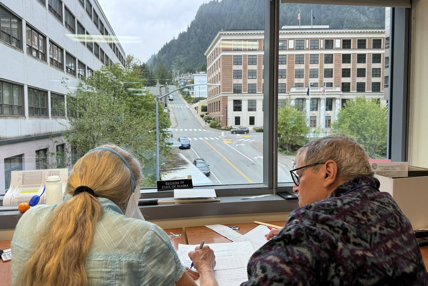 Workers at the Alaska Division of Elections’ State Review Board consider ballots on Tuesday, Aug. 27, 2024, at the division’s headquarters in Juneau. At background is the Alaska State Capitol. (James Brooks/Alaska Beacon)