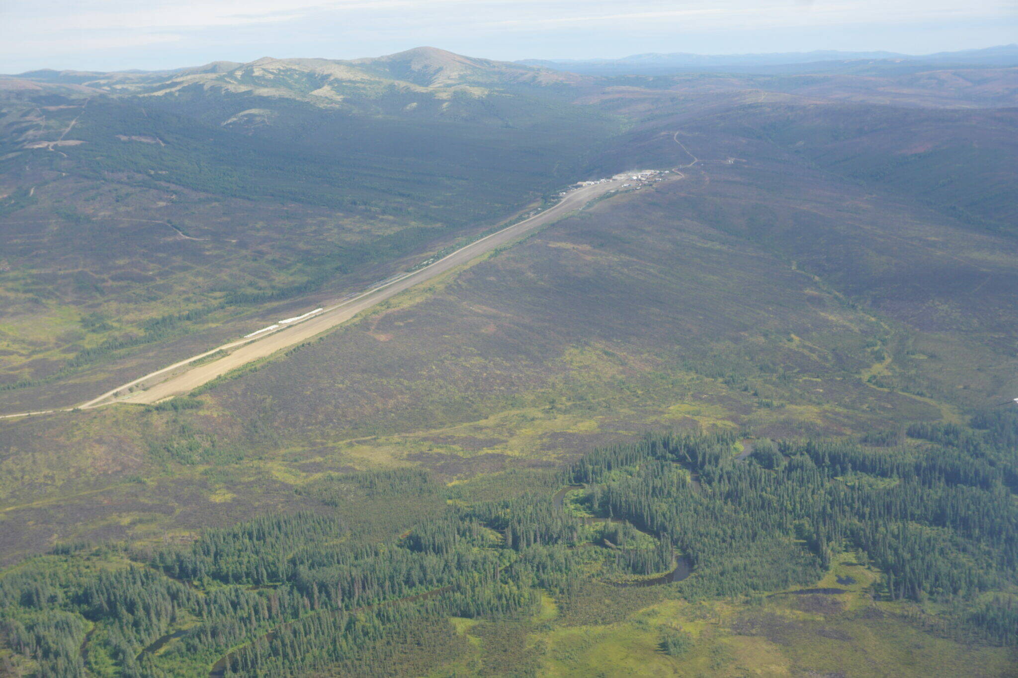 The Donlin Gold airstrip, with the camp at the far end on the right, is seen from the air on Aug. 11, 2022. The mine site is in the hilly terrain near Southwest Alaska’s winding Kuskokwim River. The mine won a key permit from the U.S. Army Corps of Engineers in 2018, but a federal judge ruled on Monday that the environmental study on which that permit was based was flawed because it failed to consider the impacts of a catastrophic dam failure. (Yereth Rosen/Alaska Beacon)