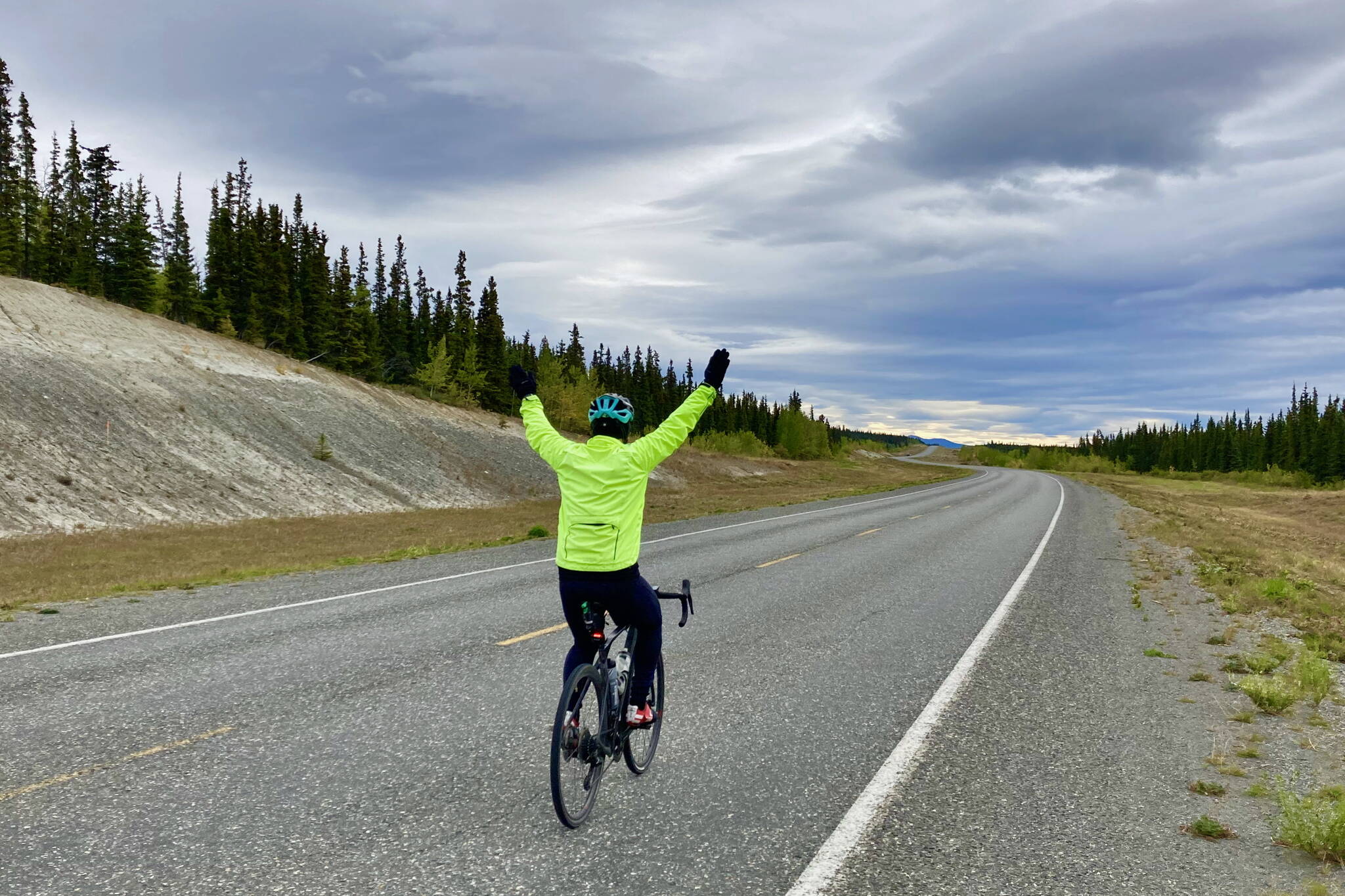 Southeast Alaska cyclist Tom Thompson raises his arms after crossing the Canadian border from British Columbia into the Yukon Territories on the Haines Road from Haines, Alaska, to Whitehorse, Yukon, Canada on Sept. 4, 2024. (Klas Stolpe / Juneau Empire)