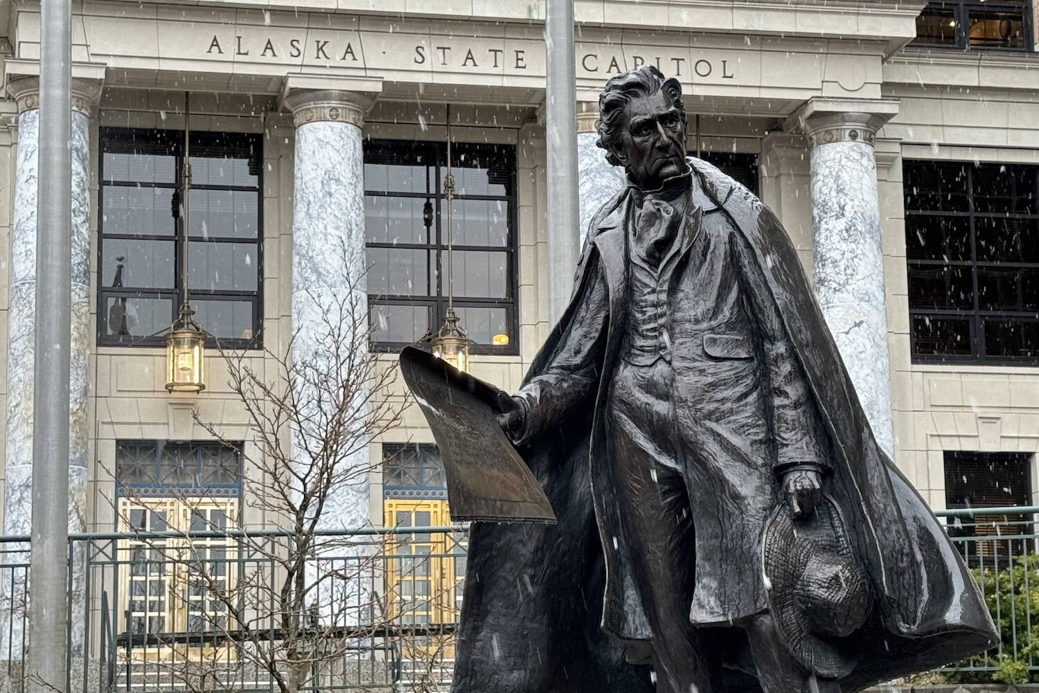 Snow falls on the Alaska Capitol and the statue of William Henry Seward on Monday, April 1, 2024. (James Brooks/Alaska Beacon)