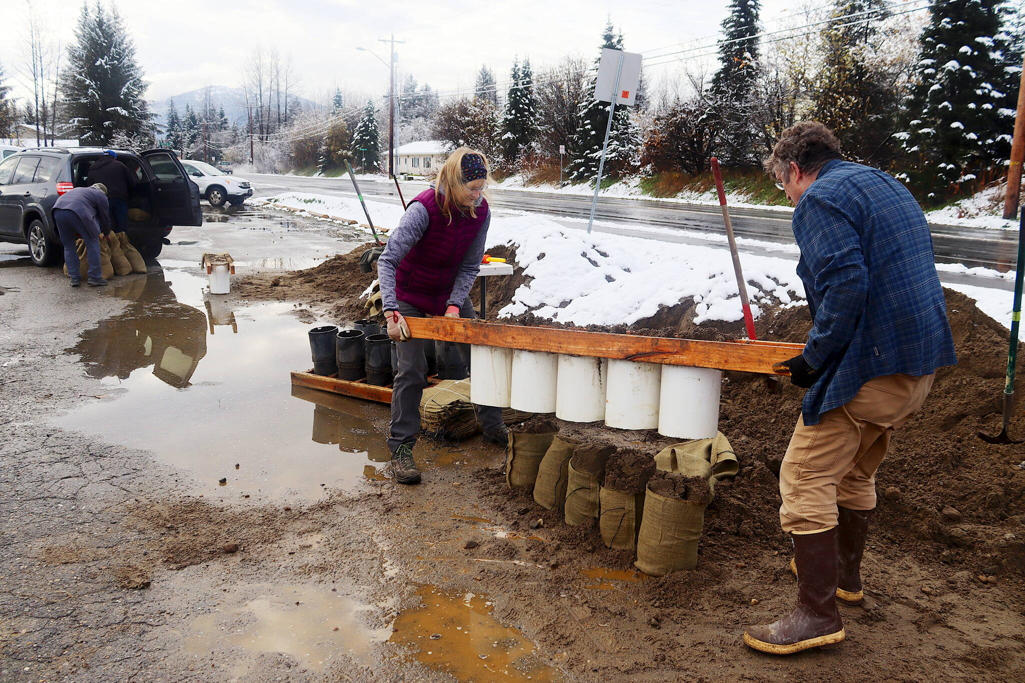 Nathan and Donna Leigh lift a tube loader off a row sandbags after filling them at Melvin Park on Saturday morning. (Mark Sabbatini / Juneau Empire)