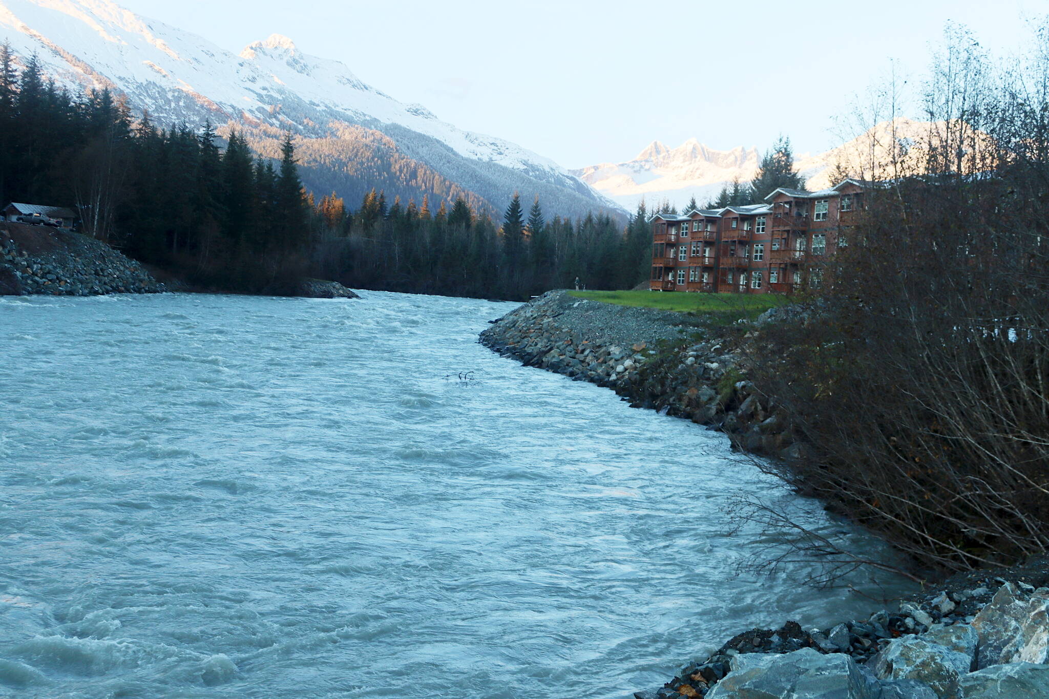 The swollen Mendenhall River flows past a condominium and other residences Sunday evening during a glacial outburst flood from Suicide Basin that crested well below the riverbanks that were reinforced with rock fill in many places following then-record flooding in August of 2023. The city is now considering installing up to four miles of Hesco barriers along one side of the river as a semi-permanent levee. (Mark Sabbatini / Juneau Empire)