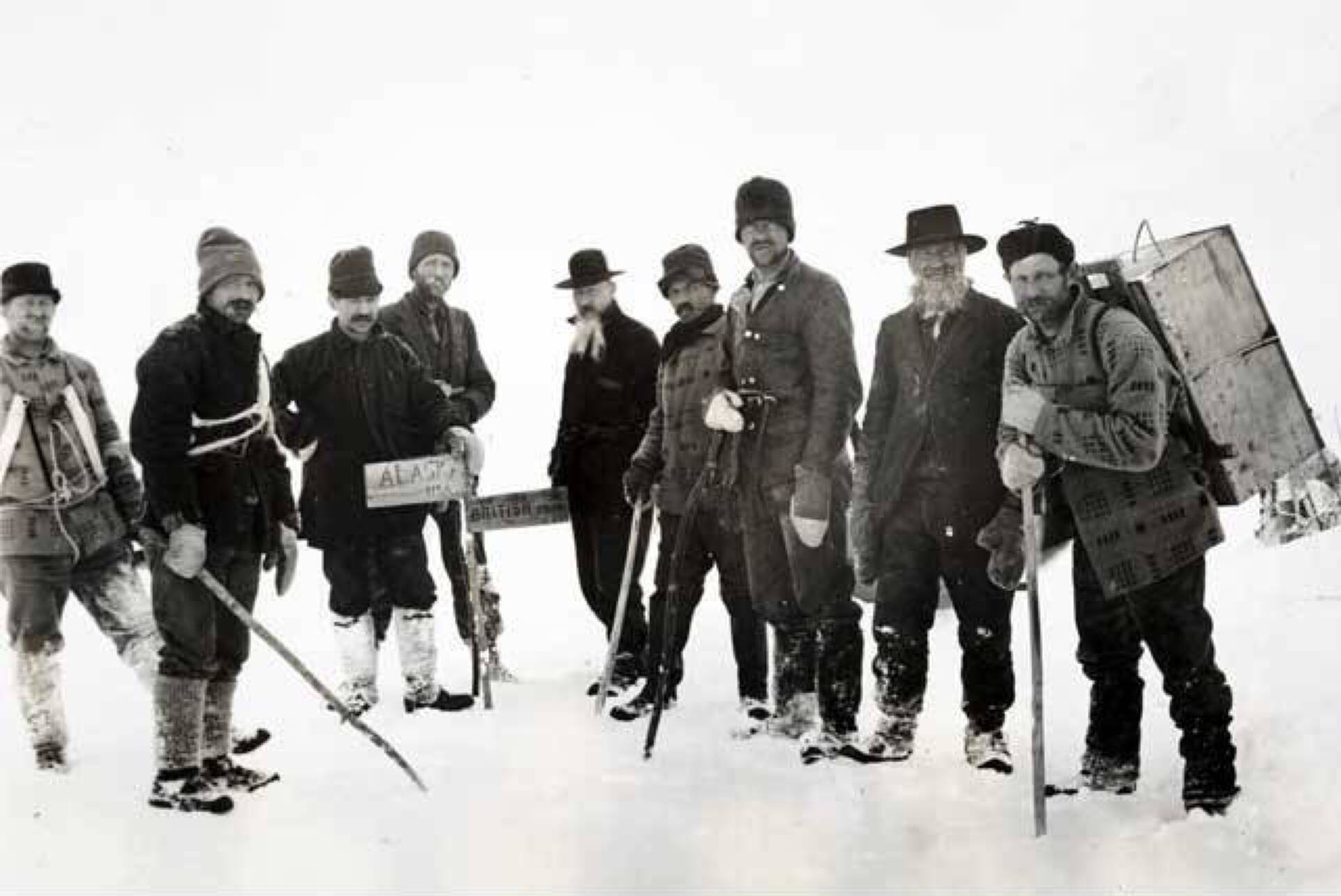 Klondike gold rush stampeders stand beside a fragile sign marking the Alaska-Canada border. (Alaska State Library historical collections ASL-P21-54)