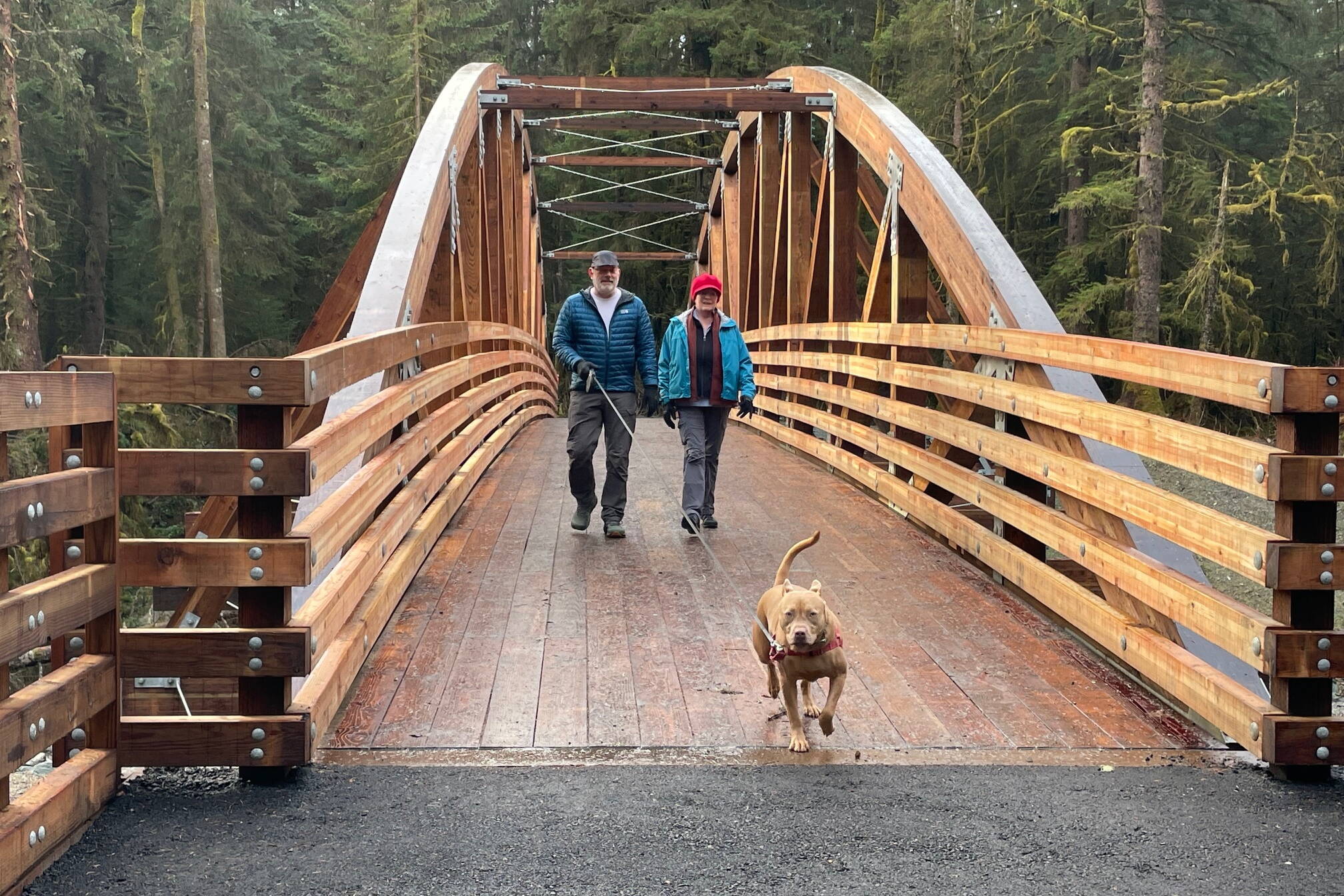 Maple the dog leads Kerry Lear and Stephanie Allison across the newly completed Kaxdigoowu Heen Dei (also known as the Brotherhood Bridge Trail) over Montana Creek Monday, November 11. (Laurie Craig / Juneau Empire)