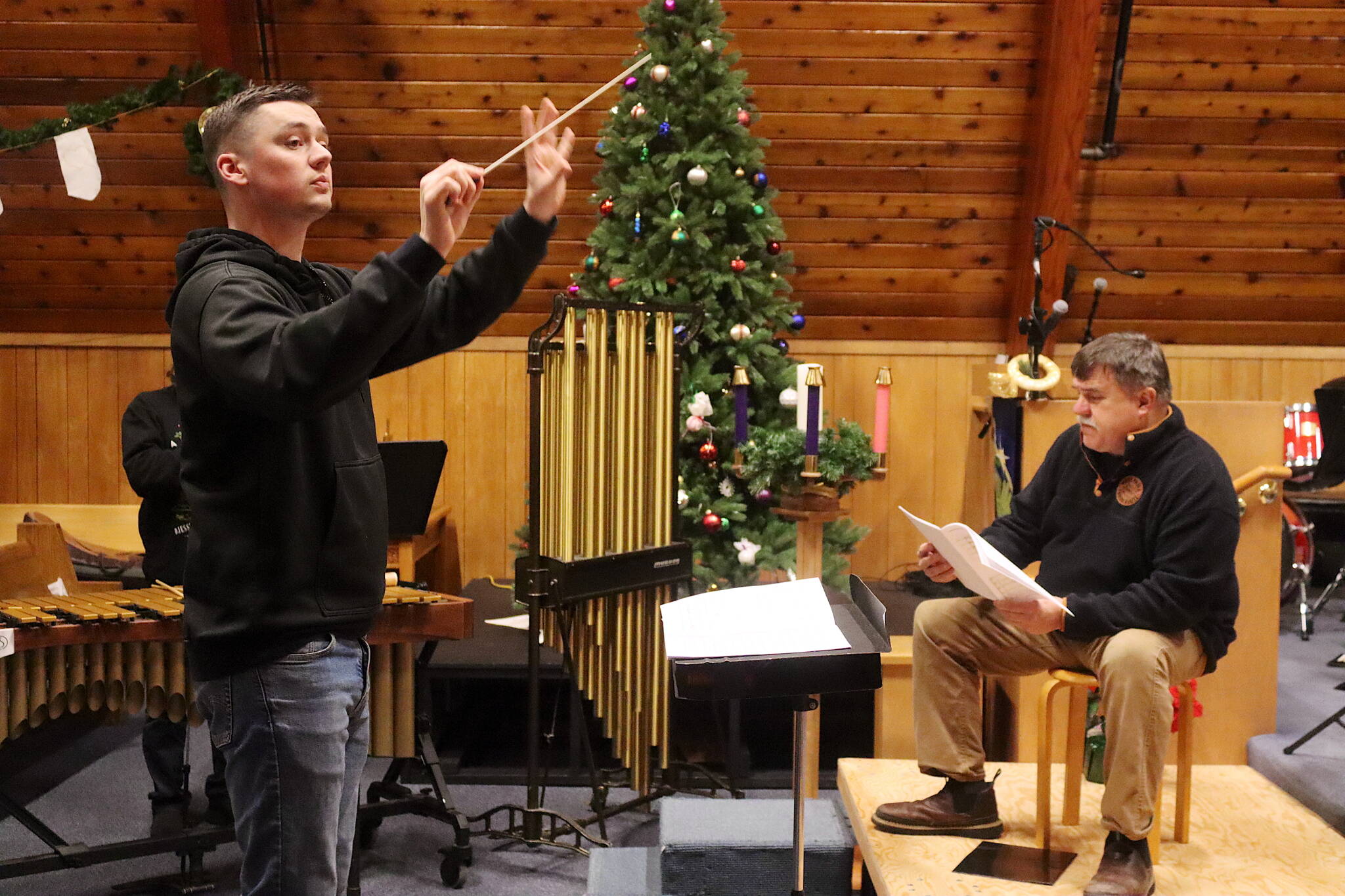 Alan Young (left) conducts while John Cooper reads the words to “The Night Before Christmas” during a rehearsal Wednesday for holiday concerts by the Taku Winds brass ensemble at K̠unéix̠ Hídi Northern Light United Church. (Mark Sabbatini / Juneau Empire)