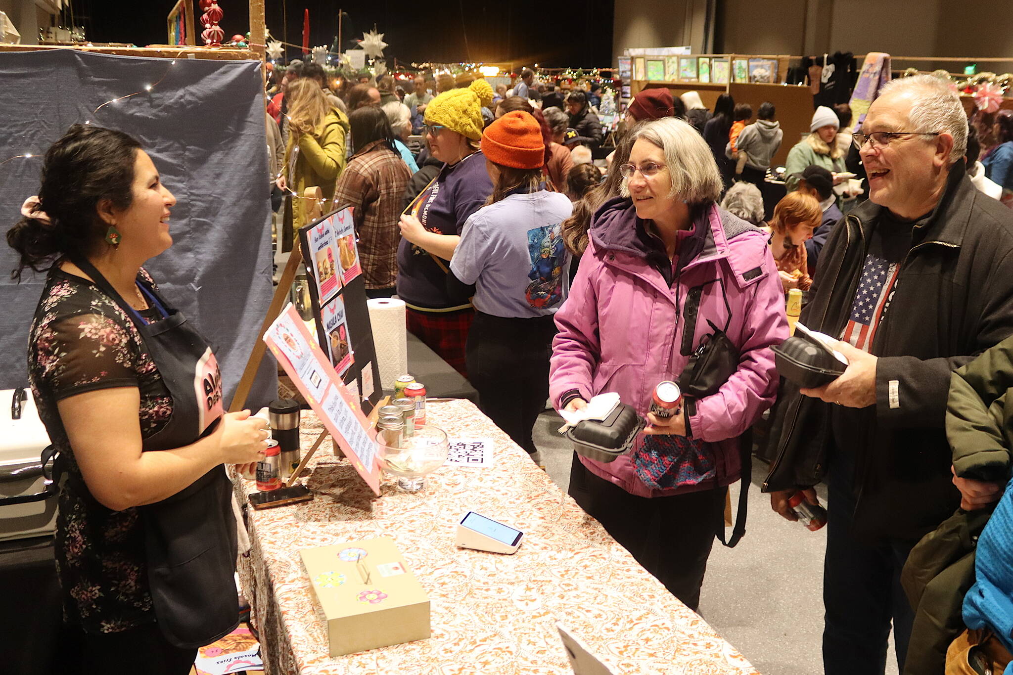 John and Laura Doogan pick up Pakistani soul food from Sara Fatimah, owner of Alaska Desi Aunty, one of the food stands at the Juneau Public Market at Centennial Hall on Friday. The market continues through Sunday. (Mark Sabbatini / Juneau Empire)