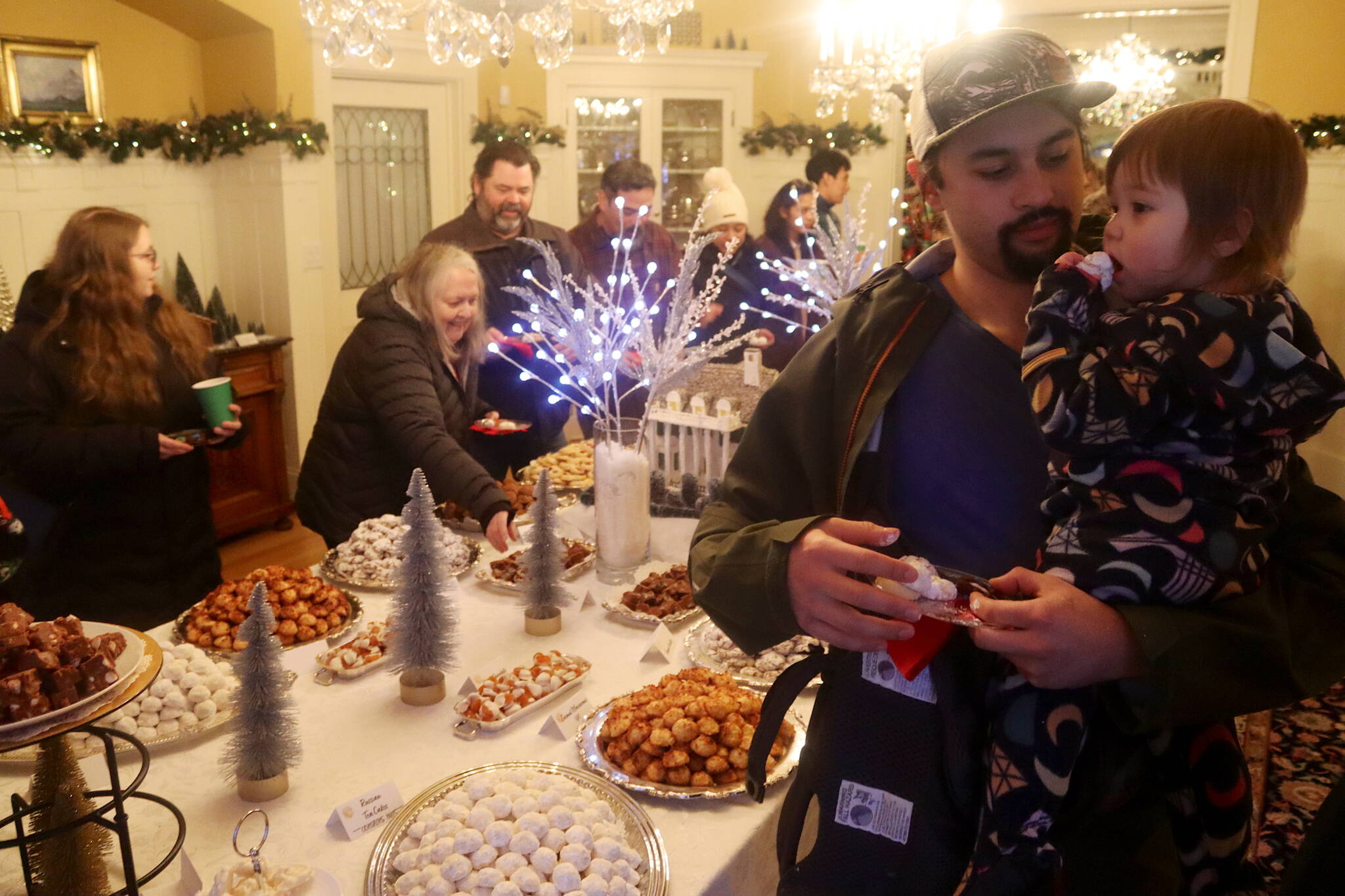 James Cheng, and his daughter Gwen, 1, help themselves to some of the 17,050 cookies being offered to visitors during the annual Holiday Open House at the Governor’s Residence on Tuesday. (Mark Sabbatini / Juneau Empire)