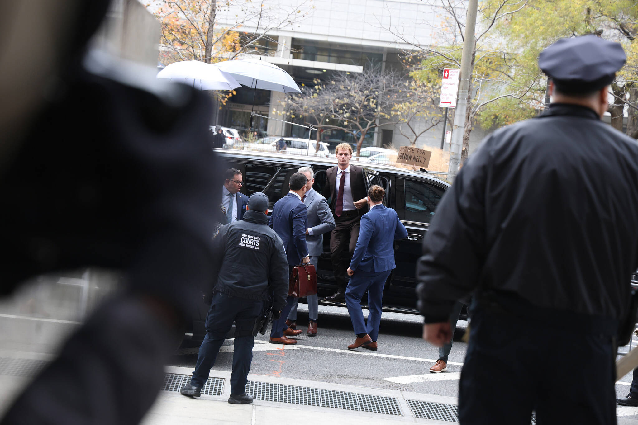 As a protester waves a sign in the background, Daniel Penny, center, accused of criminally negligent homicide in the chokehold death of Jordan Neely, arrives at State Supreme Court in Manhattan on Monday, Dec. 9, 2024. A New York jury acquitted Daniel Penny in the death of Jordan Neely and as Republican politicians hailed the verdict, some New Yorkers found it deeply disturbing.(Jefferson Siegel/The New York Times)