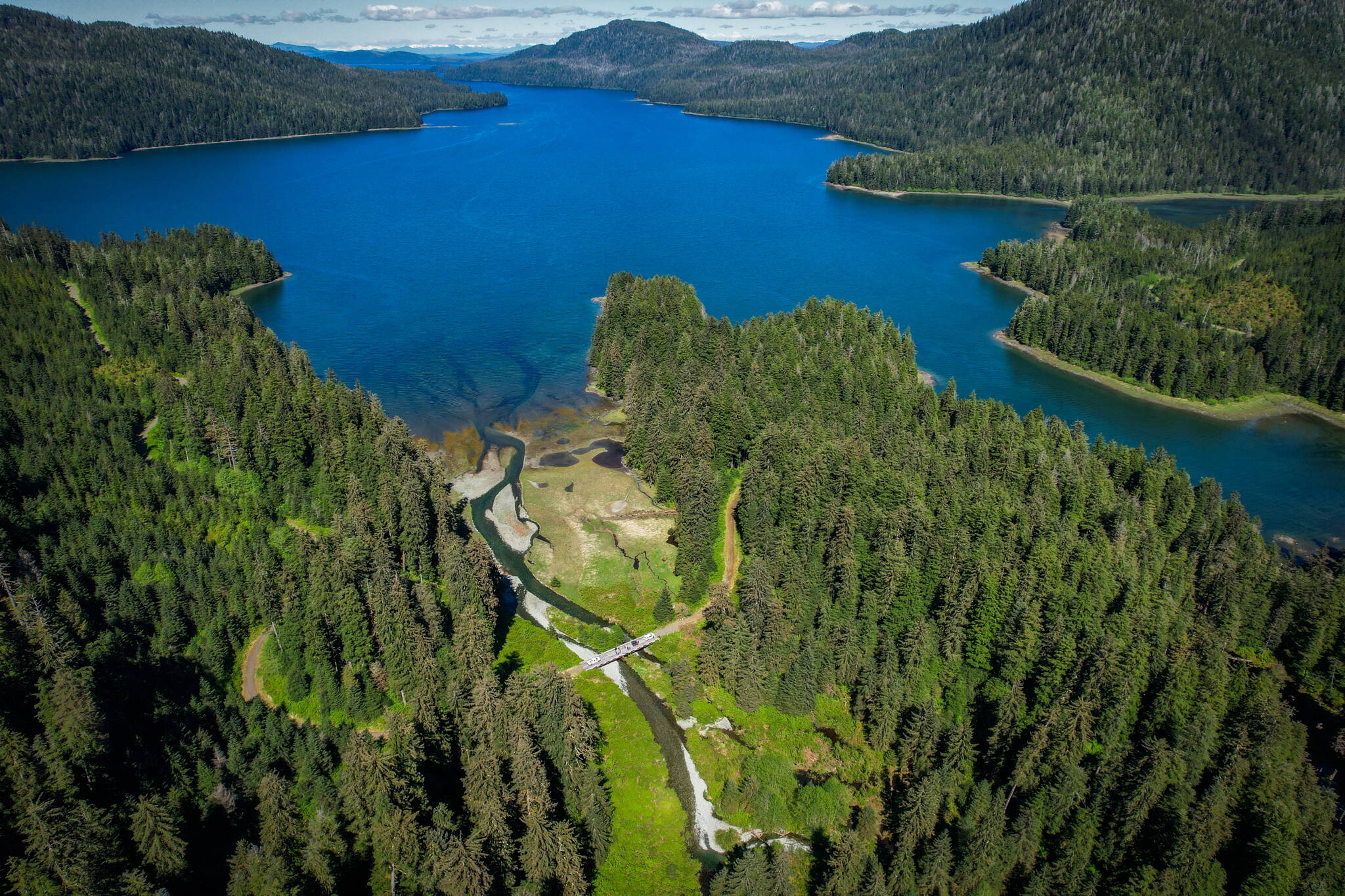 An aerial view of L’áan Yík (Channel inside or Port Camden) with cars and people gathered on the bridge over Yéil Héeni (Raven’s Creek) during a May 2024 convening on Kuiu Island. Partners that comprise the Ḵéex̱’ Ḵwáan Community Forest Partnership and staff from the Tongass National Forest met to discuss priorities for land use, stream restoration, and existing infrastructure on the north Kuiu road system. (Photo by Lee House)