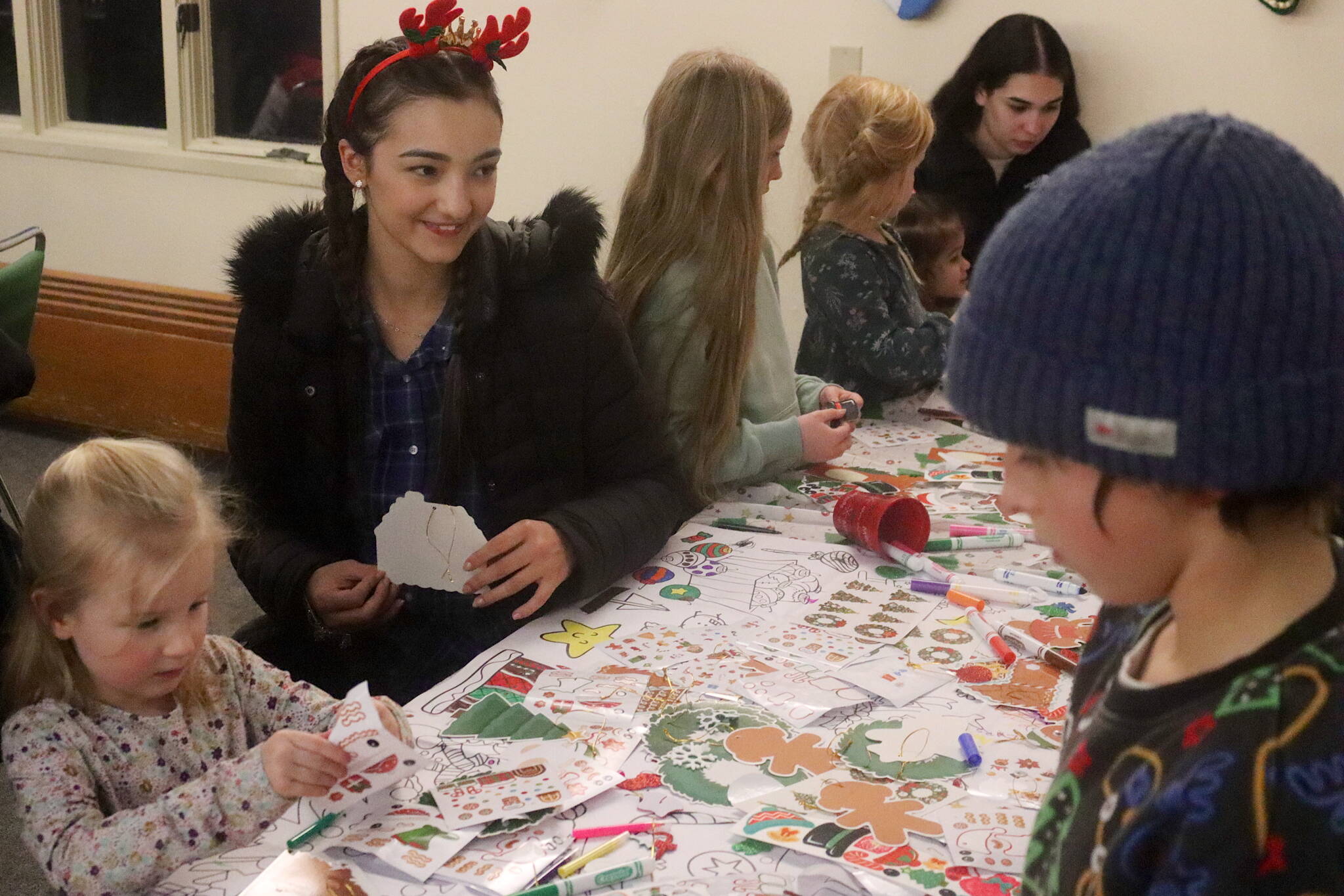 Maria Laura Guollo Martins, 22, an Eaglecrest Ski Area employee from Urussanga, Brazil, working via a J-1 student visa, helps Juneau kids make holiday decorations during the resort’s annual Christmas Eve Torchlight Parade gathering on Tuesday. (Mark Sabbatini / Juneau Empire)