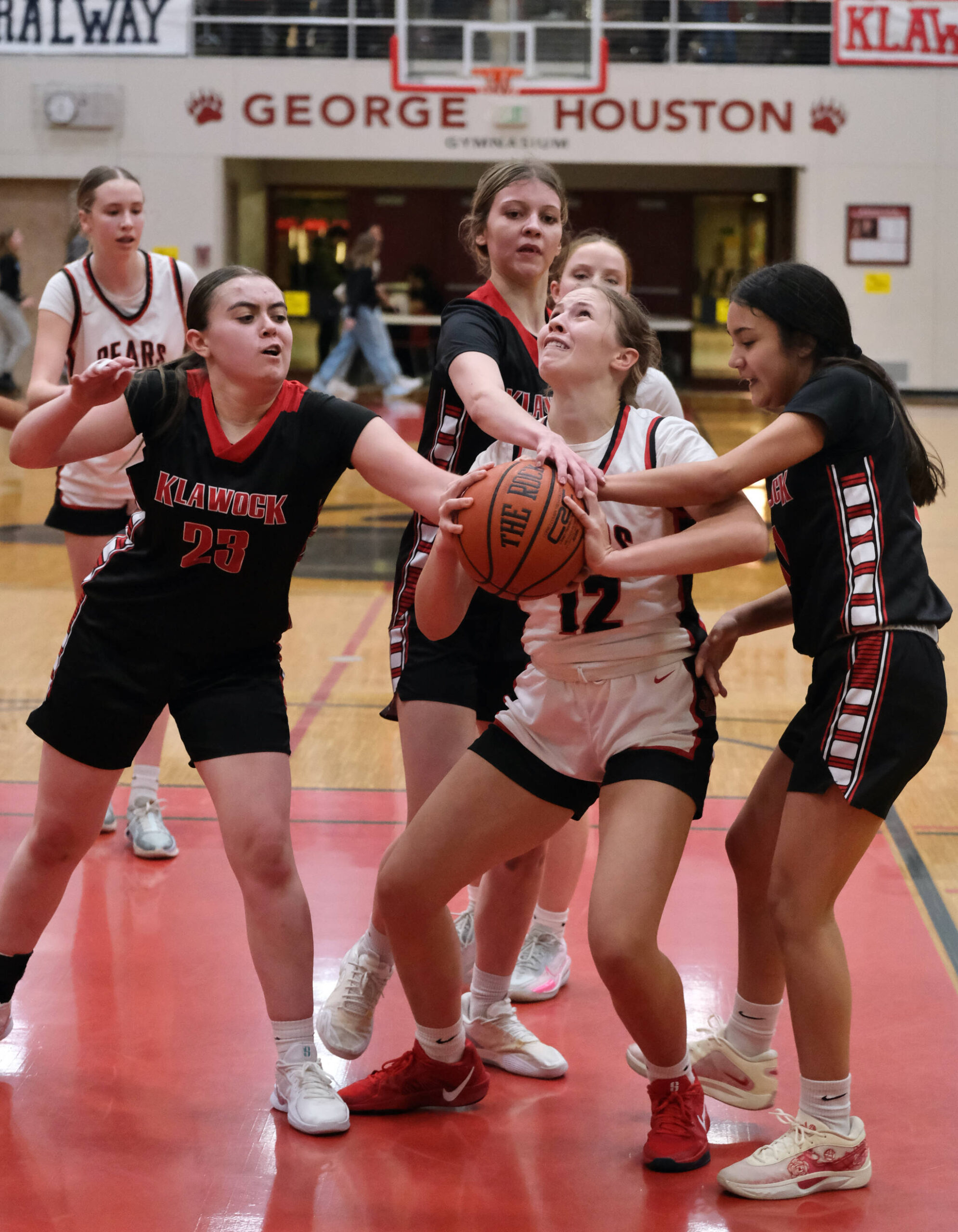 Juneau-Douglas High School: Yadaa.at Kalé Crimson Bears sophomore Bergen Erickson (12) is fouled on a shot as Klawock senior Lea Armour (23), eighth grader Jayla Edenshaw and senior Kaiya Marvin defend during the Crimson Bears 71-21 win over the Chieftains on the opening day of the George Houston Capital City Classic on Friday in Juneau. (Klas Stolpe / Juneau Empire)