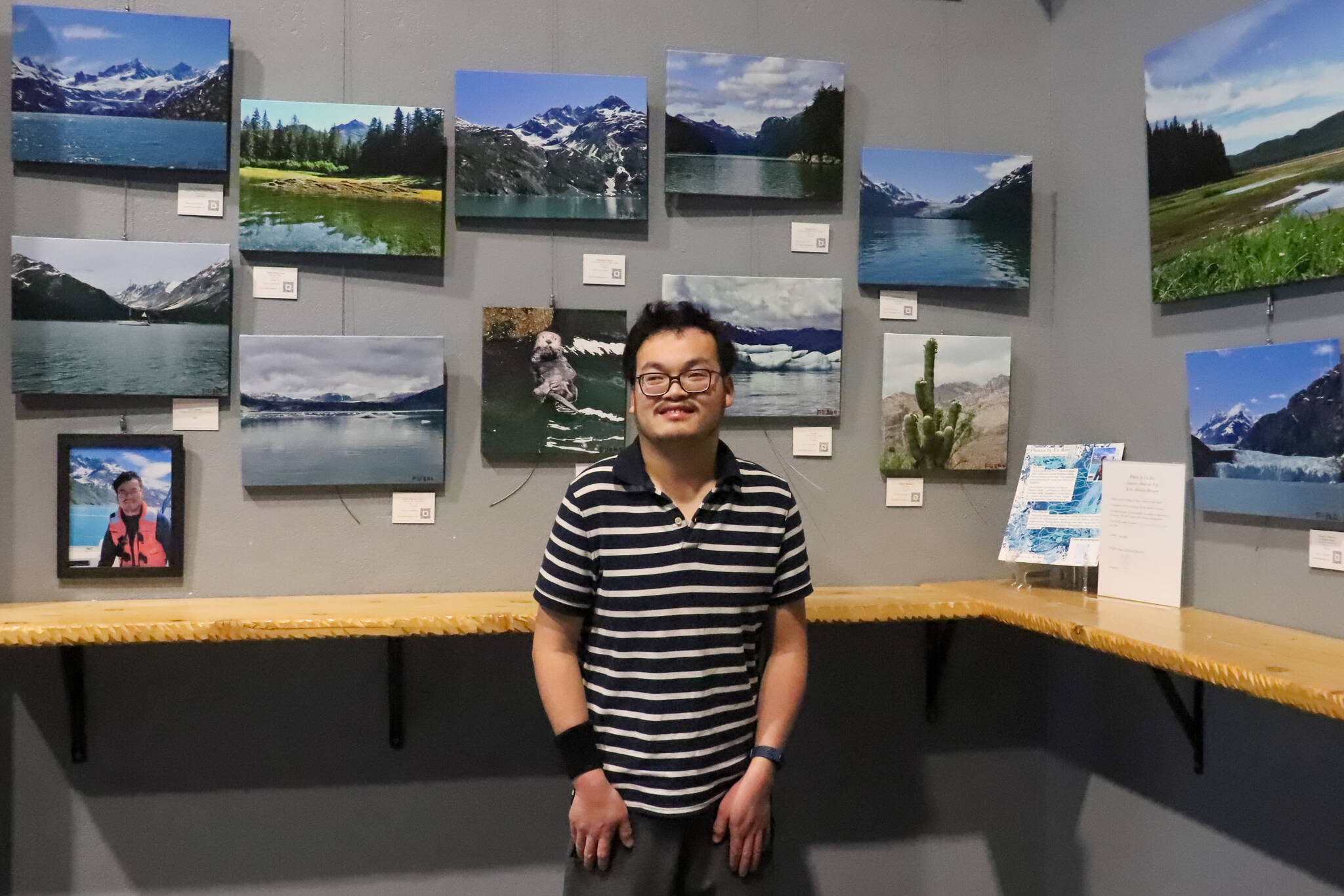 Fu Bao Hartle stands with his first solo photography exhibit at the Alaskan Brewery Tasting room on Thursday. (Jasz Garrett / Juneau Empire)