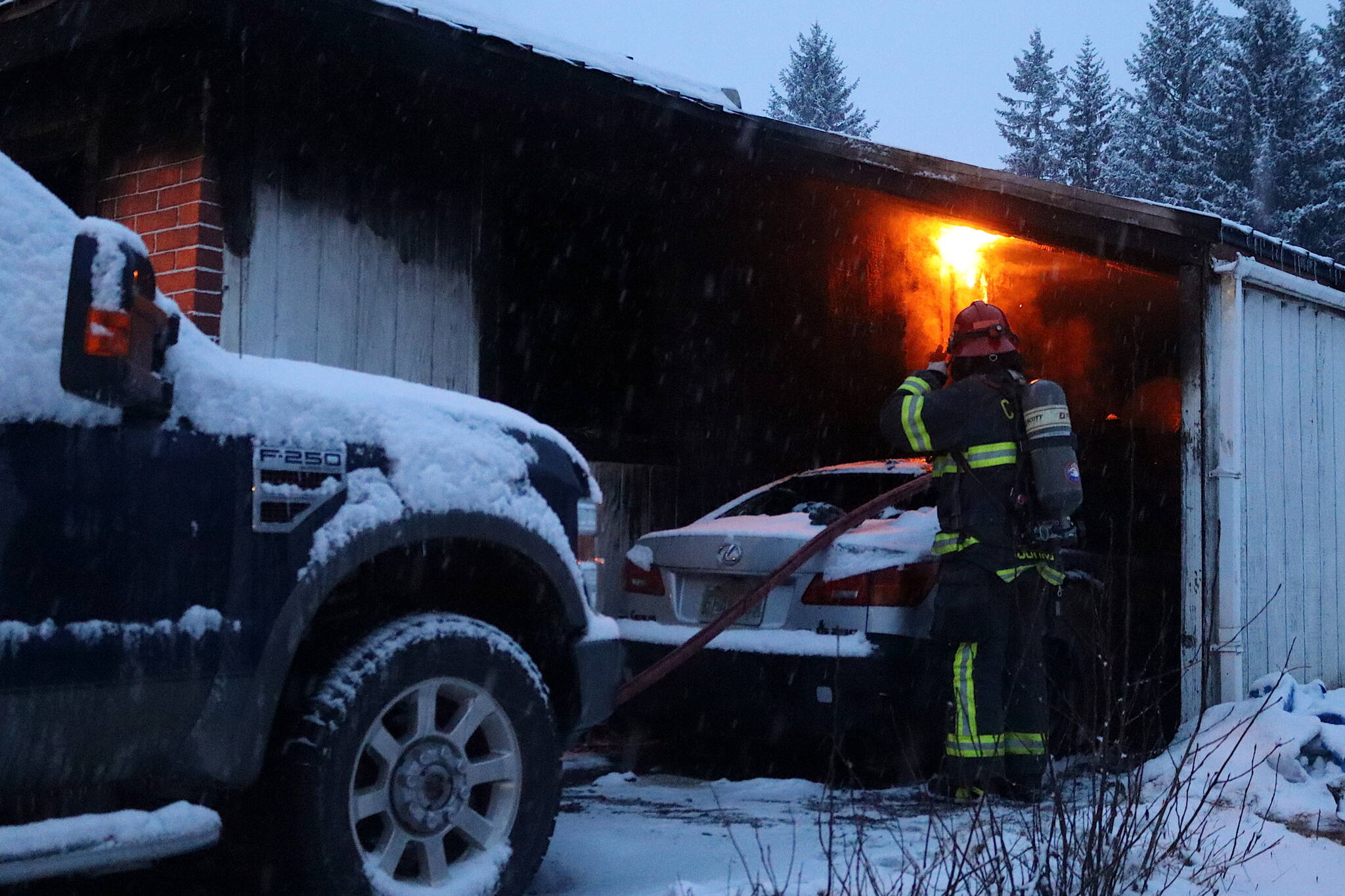 A firefighter tries to contain a flareup in a house fire on Aspen Avenue on Saturday morning. (Mark Sabbatini / Juneau Empire)