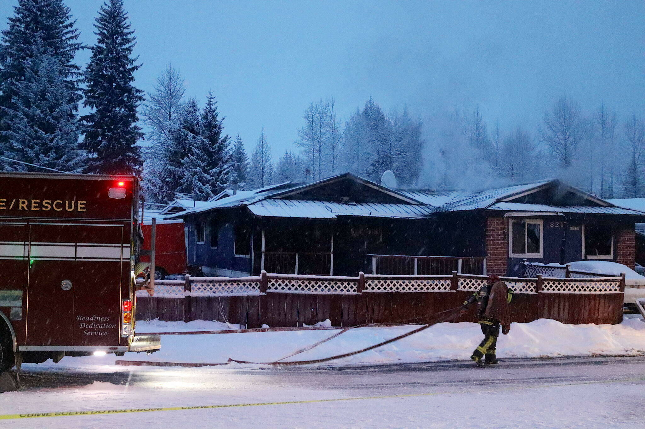 A firefighter carries a hose toward a Mendenhall Valley house still experiencing flareups hours after a fire started early Saturday morning. (Mark Sabbatini / Juneau Empire file photo)