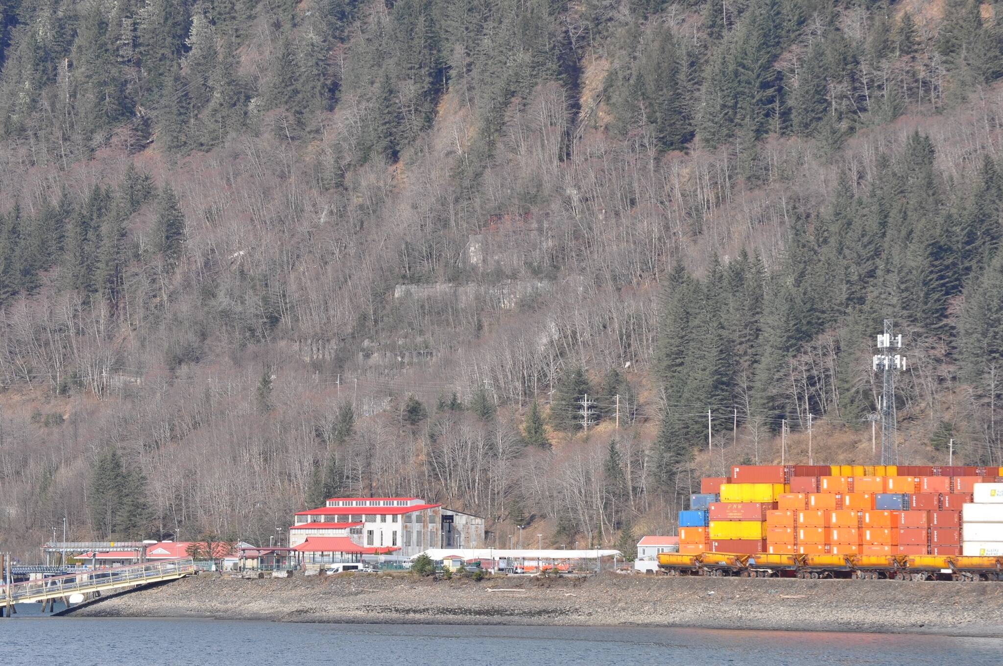 Ruins of the Alaska-Juneau Gold Mine mill are visible through leafless trees above the red roofed steam plant near Alaska Marine Lines’ containers stacked at the rock dump in this April 3, 2024, photo taken from Douglas Island. (Laurie Craig / Juneau Empire)