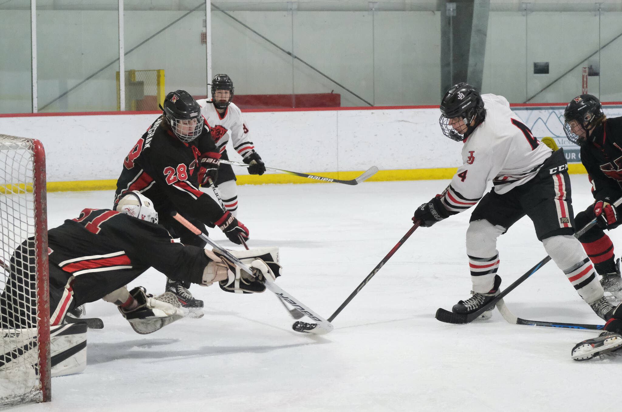 Juneau-Douglas High School: Yadaa.at Kalé senior Luke Bovitz (4) and Kenai’s Evyn Witt (31) and Cole Langham (28) go for a puck during the Crimson Bears’ 5-1 loss to the Kardinals on Saturday at Treadwell Ice Arena. (Klas Stolpe / Juneau Empire)