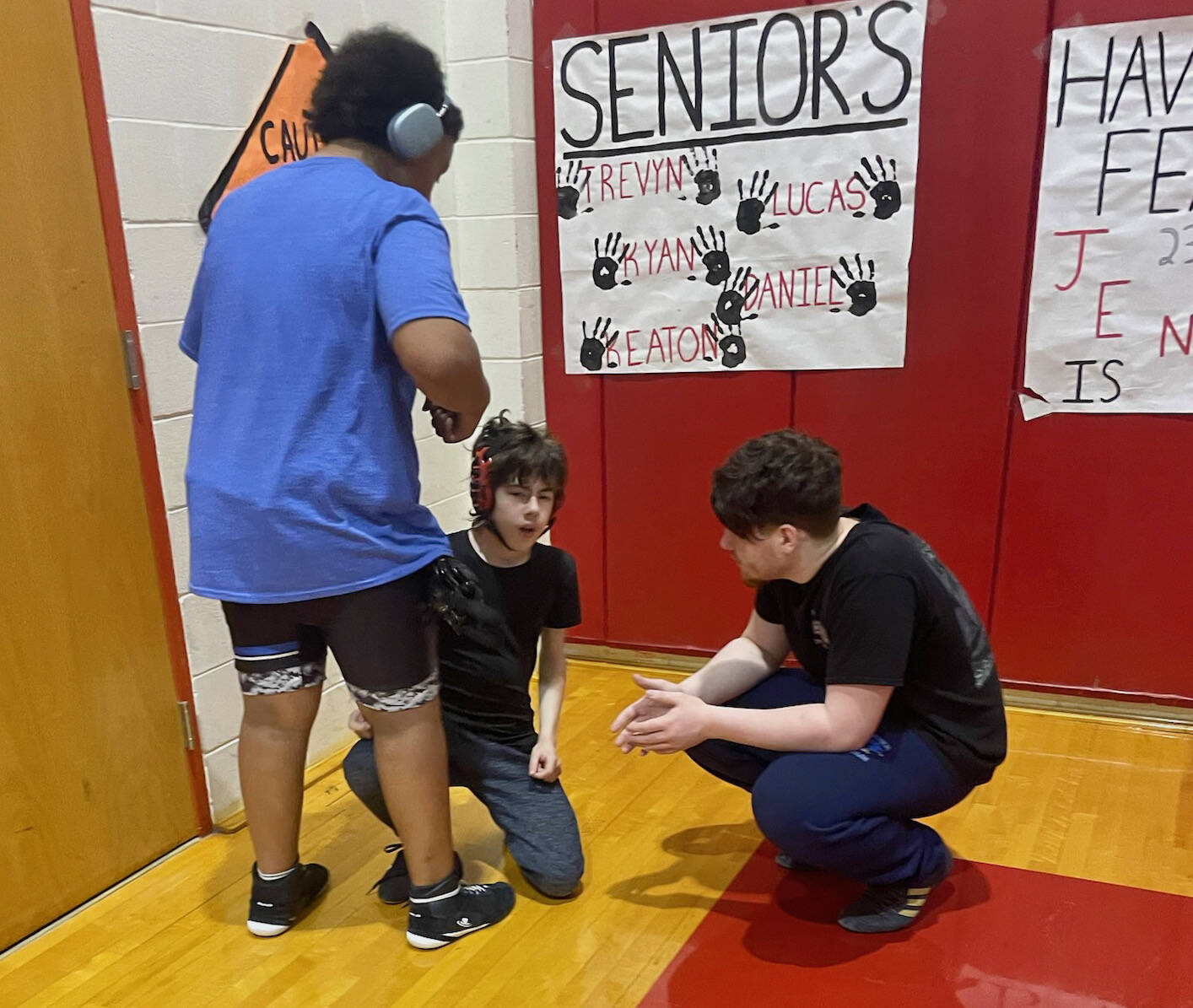 Thunder Mountain Middle School heavyweights Braedon-Lee Atrim and Barron Marexo help first-year wrestler Tanner Freebury prepare for his match in Wrangell Saturday. (Photo courtesy TMMS)