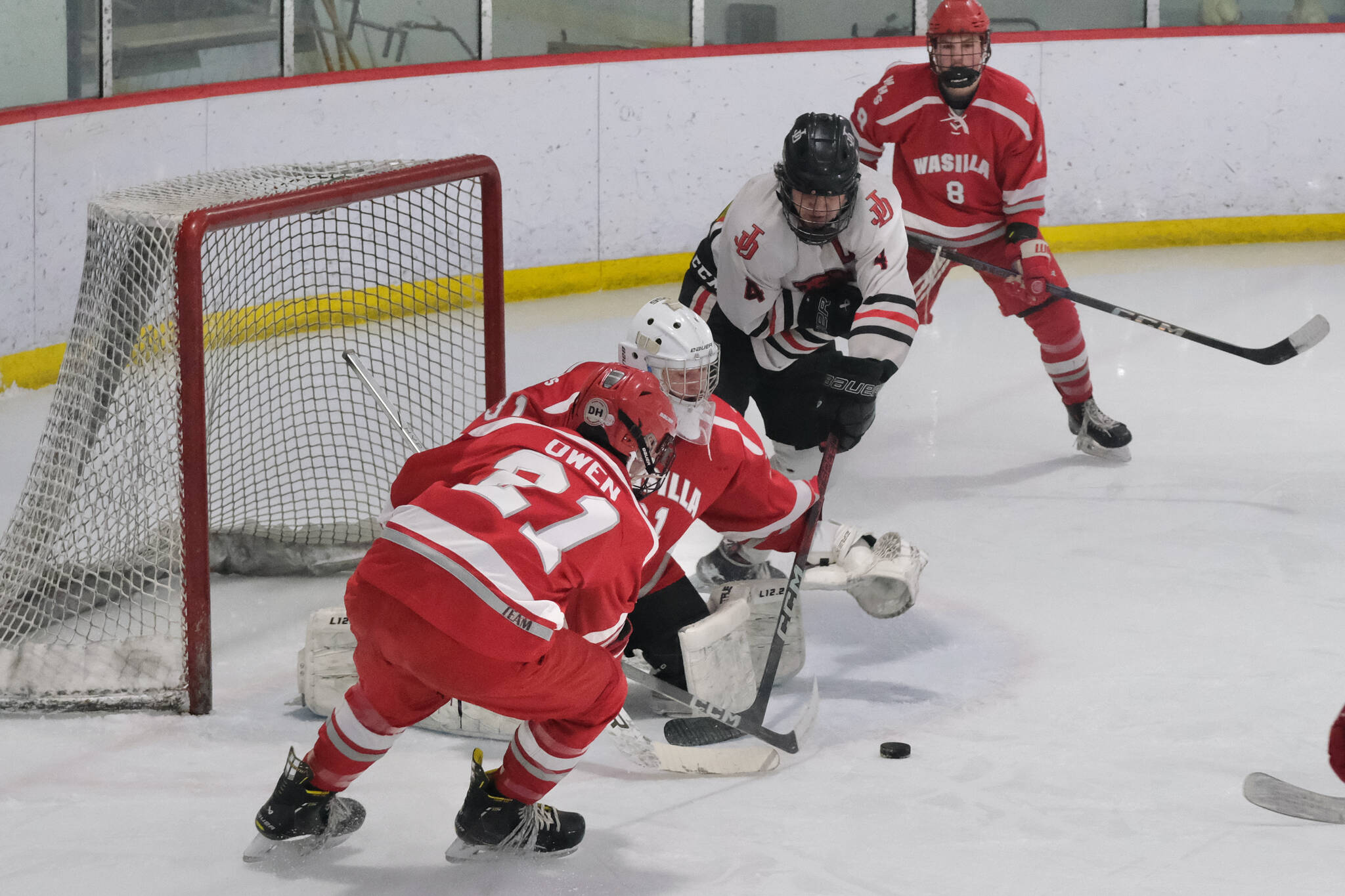 Juneau-Douglas High School: Yadaa.at Kalé senior Luke Bovitz (4) battles for a goal against Wasilla juniors Evan Owen (21), goalie Carson Branholm (31) and Chase Malstrom (8) during the Crimson Bears’ 3-1 win over the Warriors at Treadwell Ice Arena on Saturday. (Klas Stolpe / Juneau Empire)