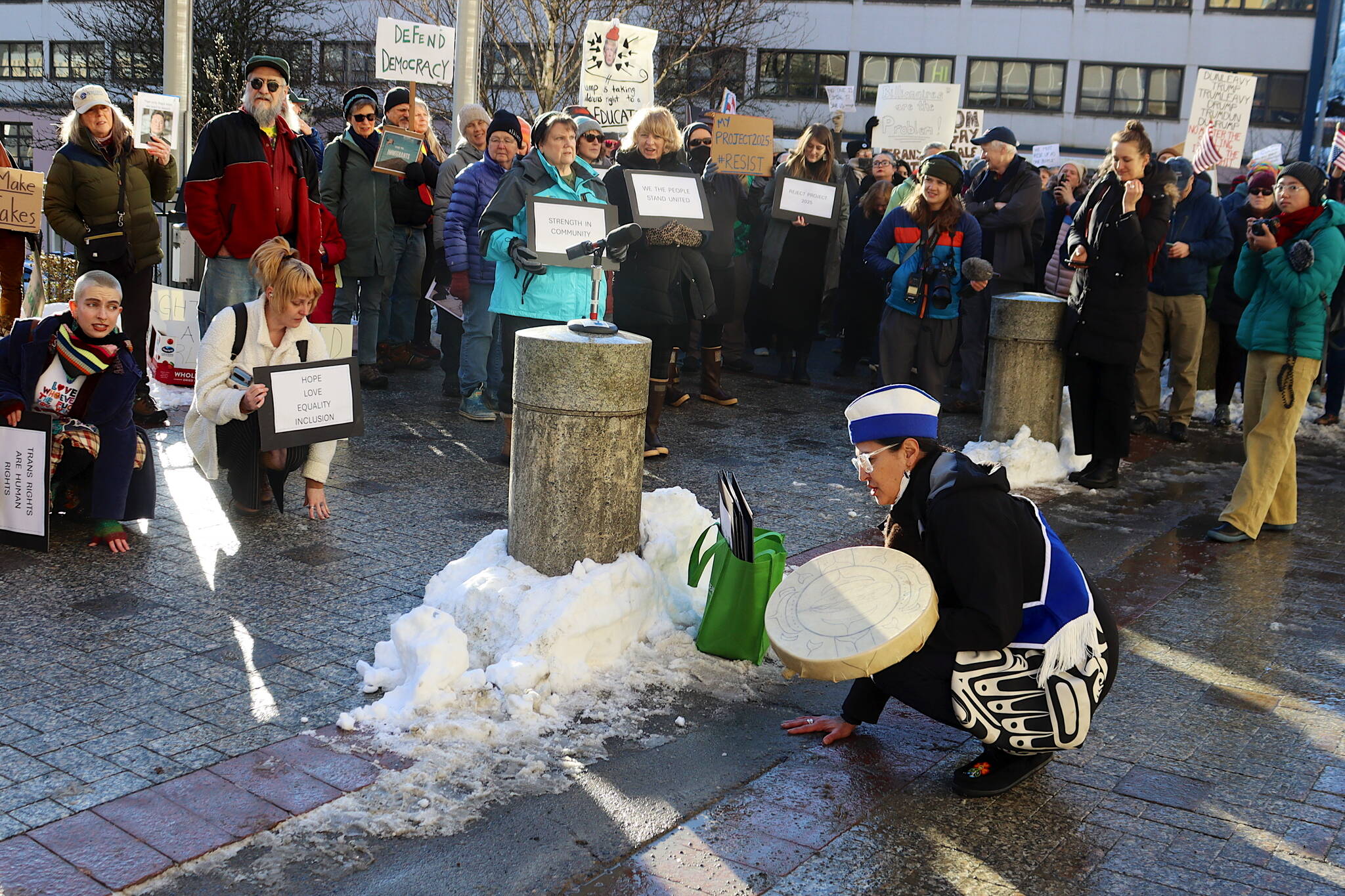 Jamiann S’eiltin Hasselquist asks participants to kneel as a gesture to “stay grounded in the community” during a protest in front of the Alaska State Capitol on Wednesday focused on President Donald Trump’s actions since the beginning of his second term. (Mark Sabbatini / Juneau Empire)