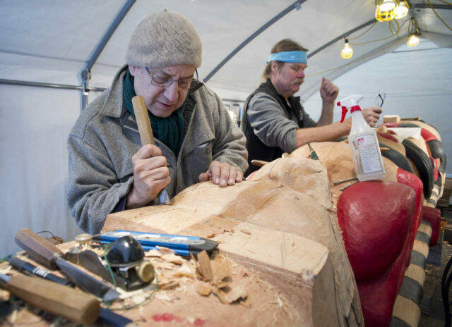 Lead carver Mick Beasley, left, and carver Fred Fulmer work on a healing totem pole at Harborview Elementary School through the summer of 2016. The totem will be erected at Gastineau Elementary School as a remembrance of the Tlingit graves the school was built on. (Juneau Empire file photo)