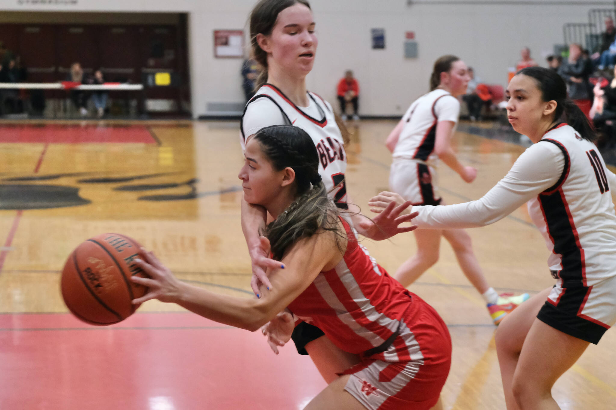 Wasilla junior Katie Jackson drives and passes around Juneau-Douglas High School: Yadaa.at Kalé seniors Cailynn Baxter and Addison Wilson (10) during the Warriors’ 65-34 win Friday over the Crimson Bears in the George Houston Gymnasium. (Klas Stolpe / Juneau Empire)