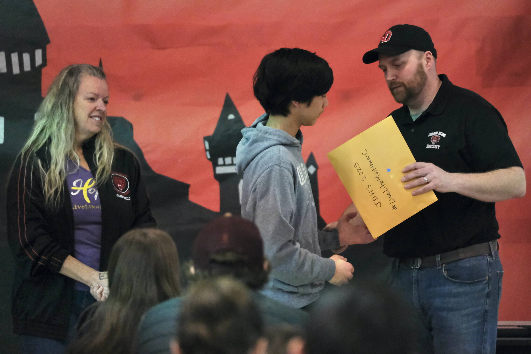 Juneau-Douglas High School: Yadaa.at Kalé hockey coach Matt Boline presents JDHS junior Nolan Cruz with the #LiveLikeMatthewC Award during the Crimson Bears hockey banquet Sunday in the JDHS commons. Matthew’s mother Judy Campbell, at left, spoke to the attendees. (Klas Stolpe / Juneau Empire)